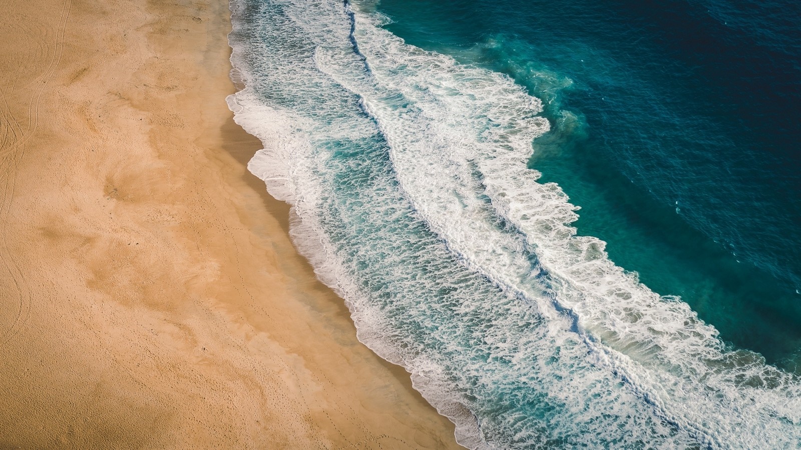 Aerial view of a sandy beach with ocean waves HD Wallpaper