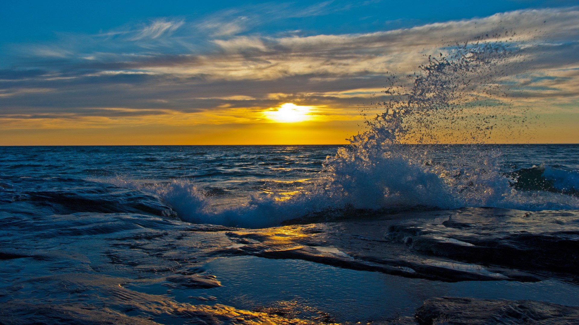 Sunset over the ocean with crashing waves on rocks HD Wallpaper