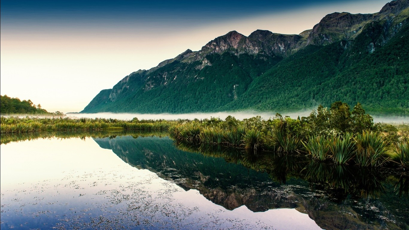 Misty mountains reflected in a calm lake at sunrise HD Wallpaper
