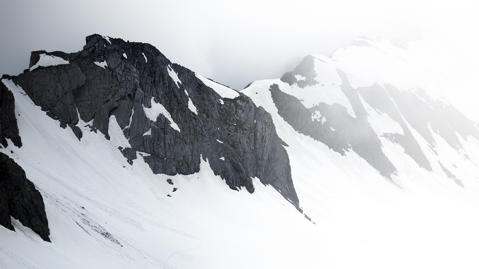Snow-covered mountains with dark rock formations HD Wallpaper
