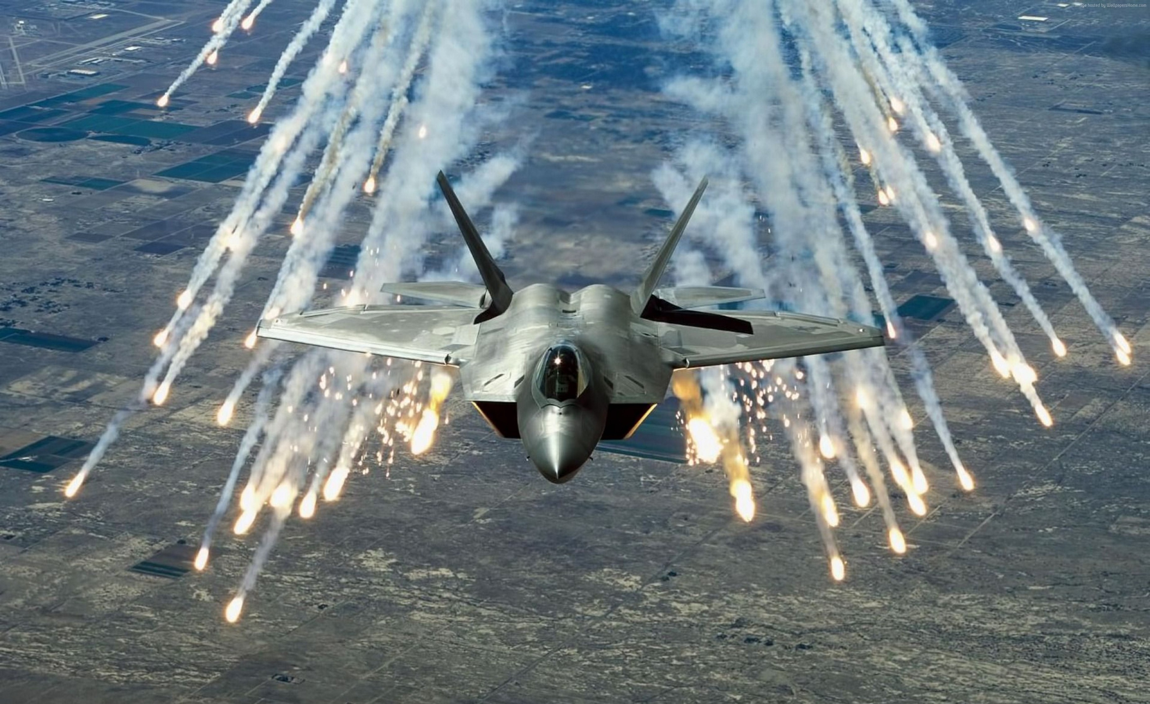 F-22 Raptor releasing flares over a landscape HD Wallpaper