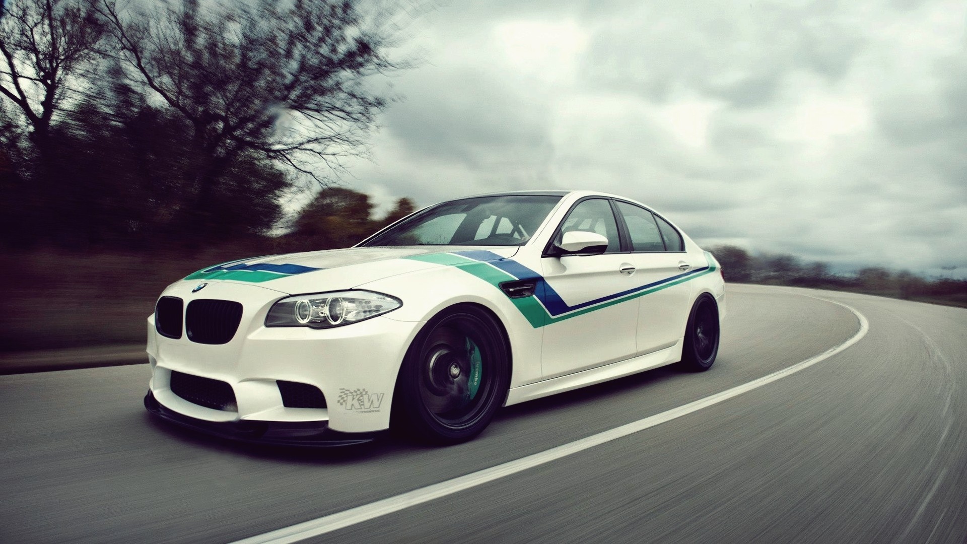 White BMW M5 Sedan with racing stripes driving on a road HD Wallpaper