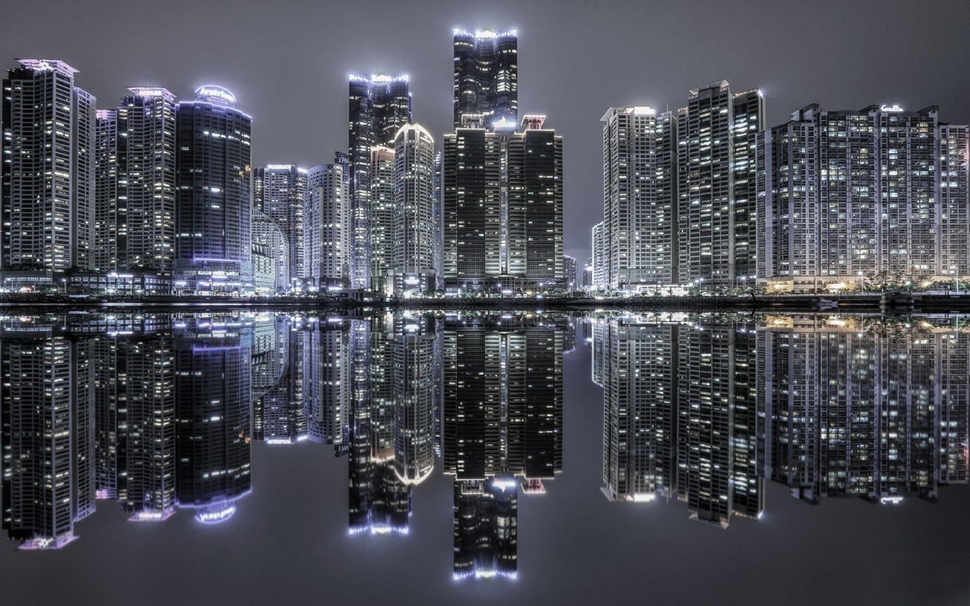 Cityscape with illuminated skyscrapers reflecting in water at night HD Wallpaper