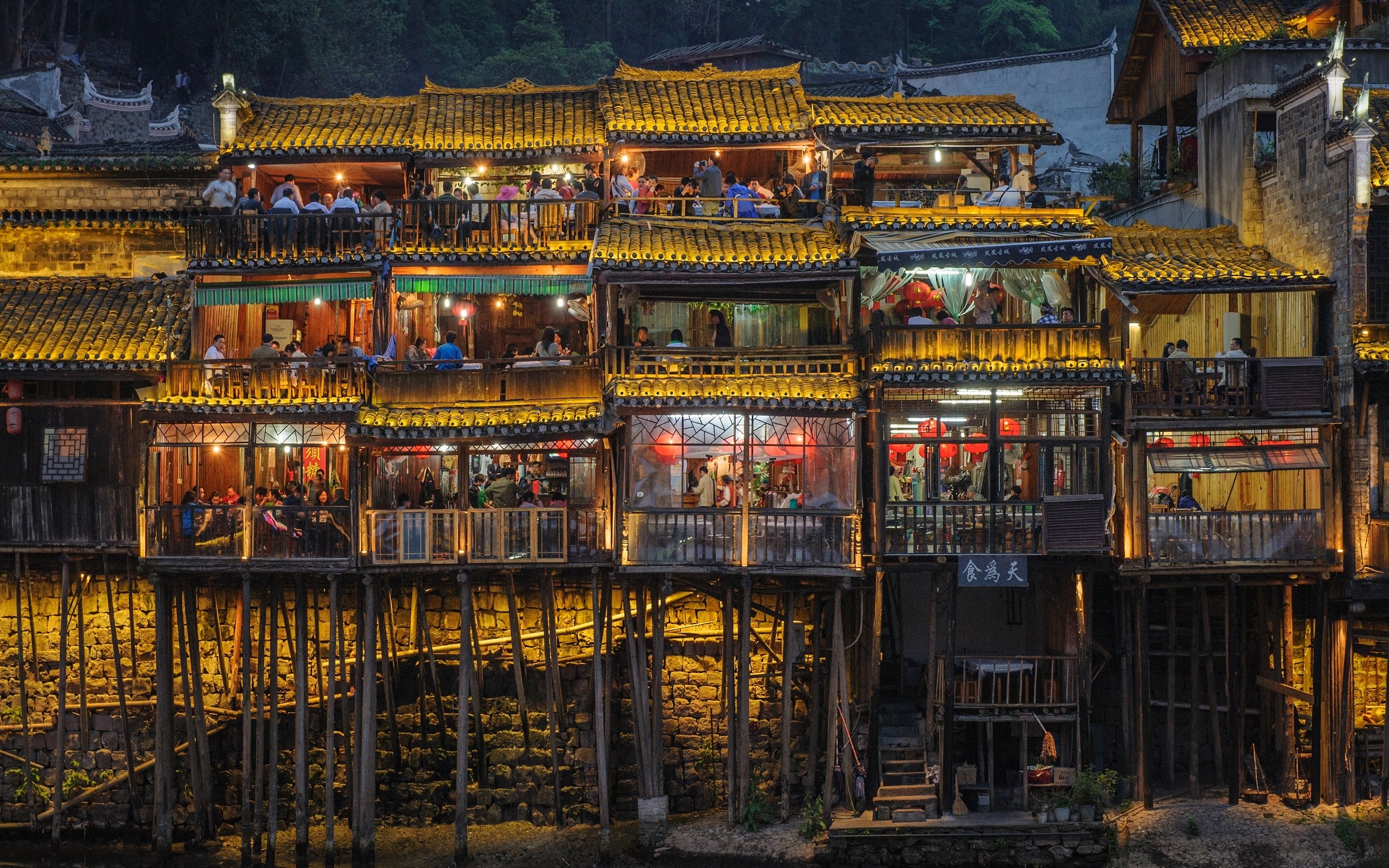 Buildings on stilts with people dining at night HD Wallpaper