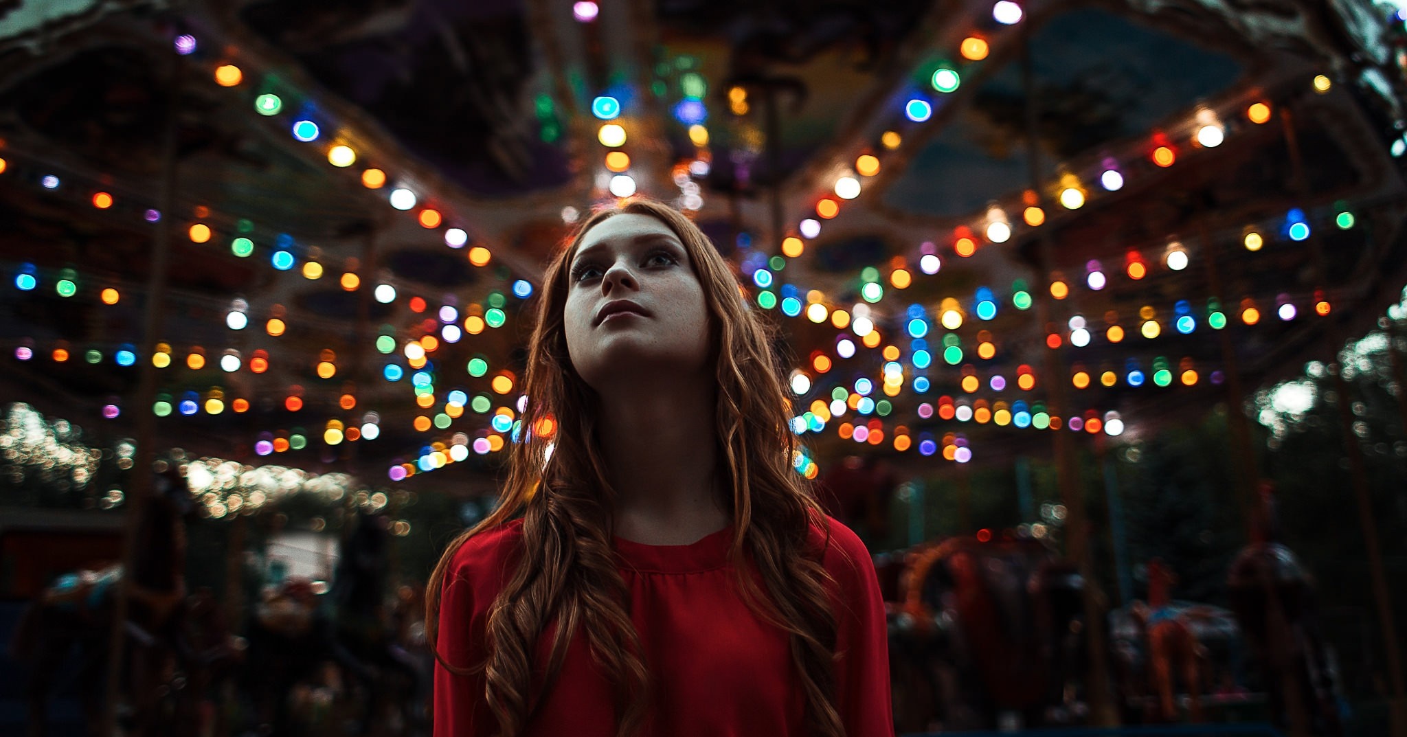 Woman looking up at colorful carousel lights at night HD Wallpaper