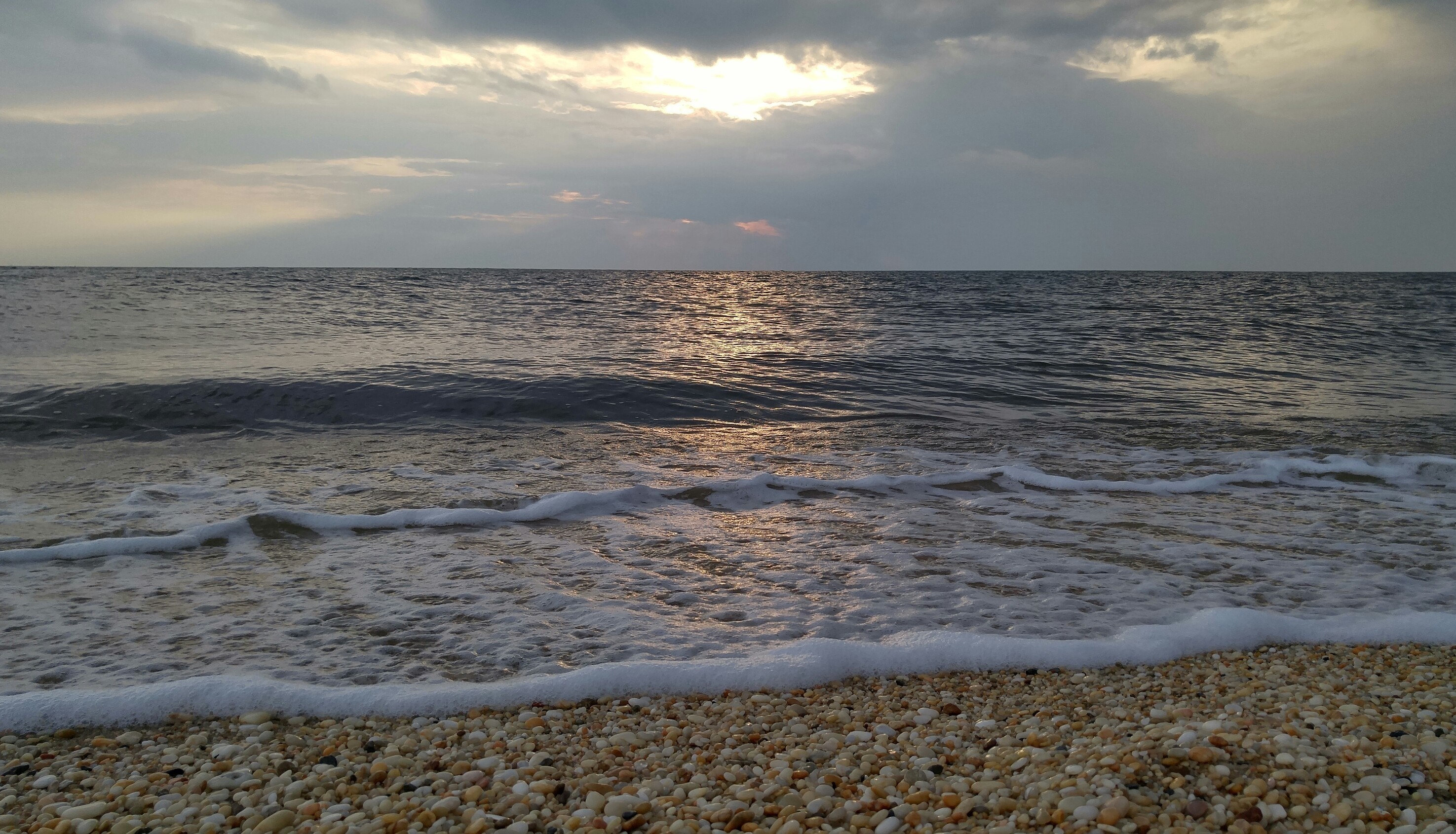 Sunset over the ocean with waves crashing on a pebble beach HD Wallpaper
