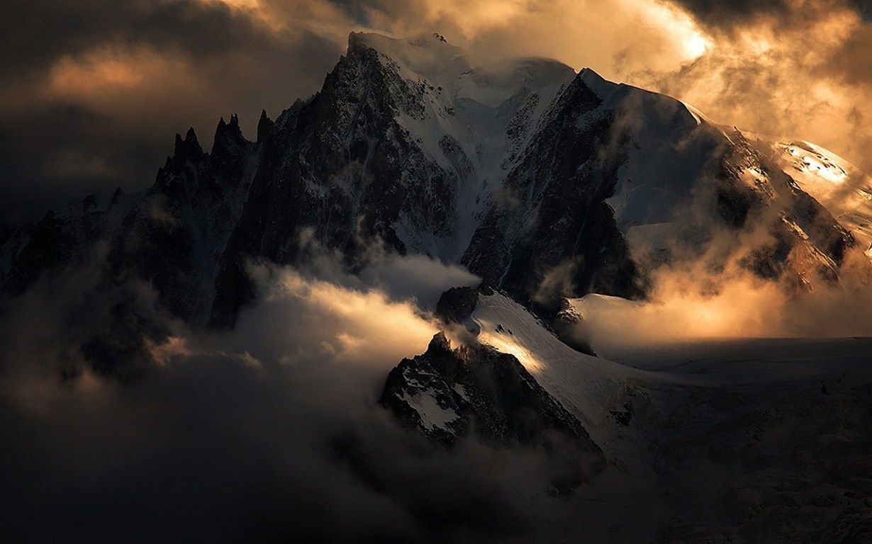 Golden sunlight breaking through clouds over snowy mountains HD Wallpaper