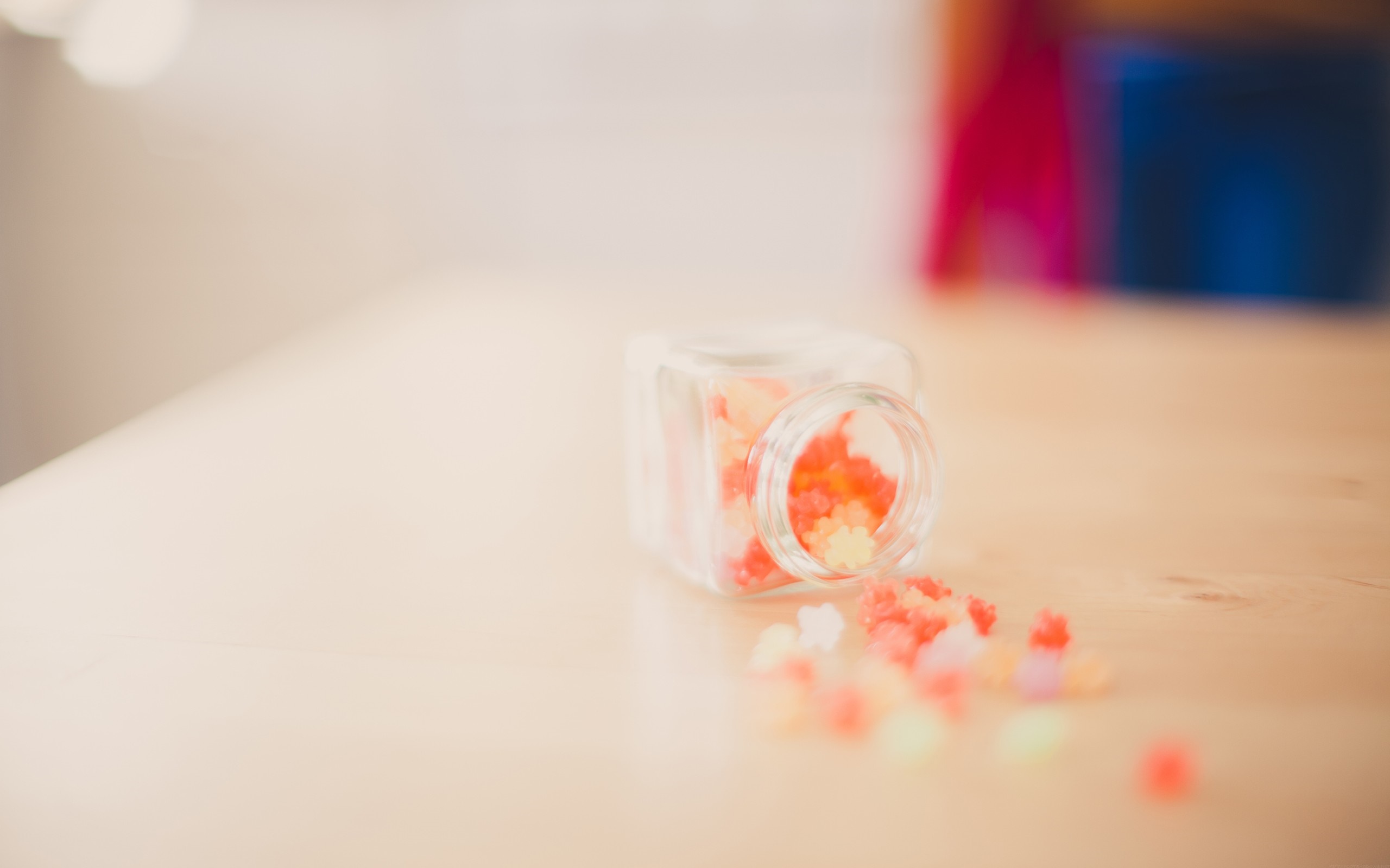 Small glass jar with colorful candies spilled on a wooden table HD Wallpaper