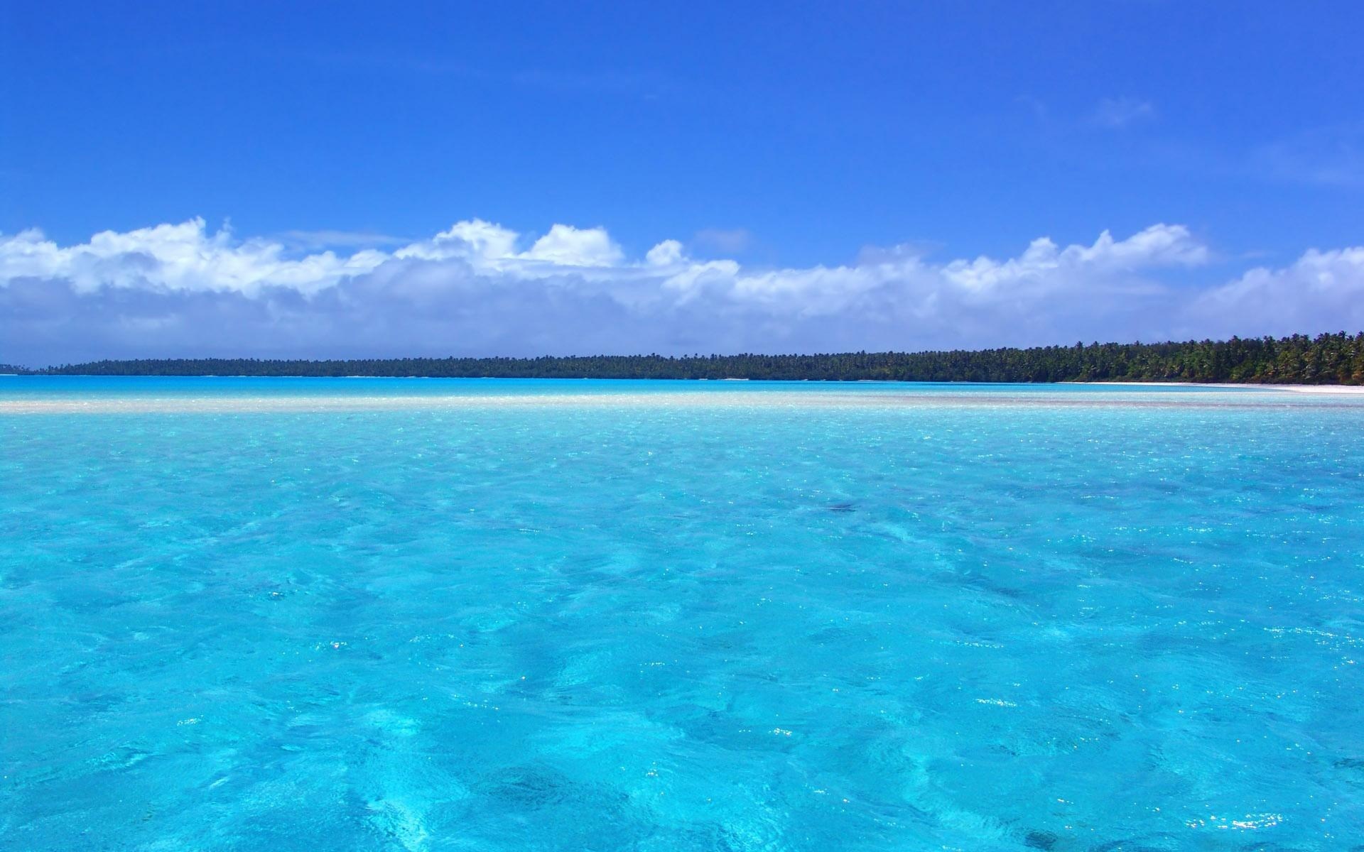 Turquoise ocean water with a distant island and blue sky HD Wallpaper