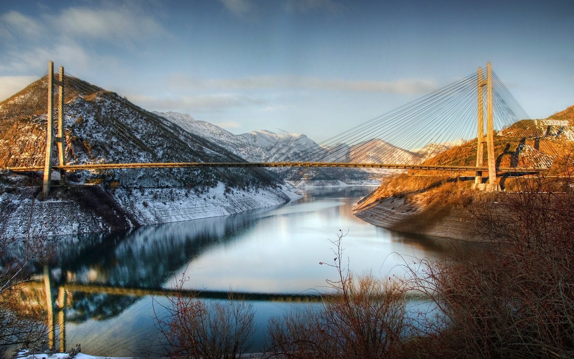 Cable-stayed bridge over a reservoir in a snowy mountain landscape HD Wallpaper