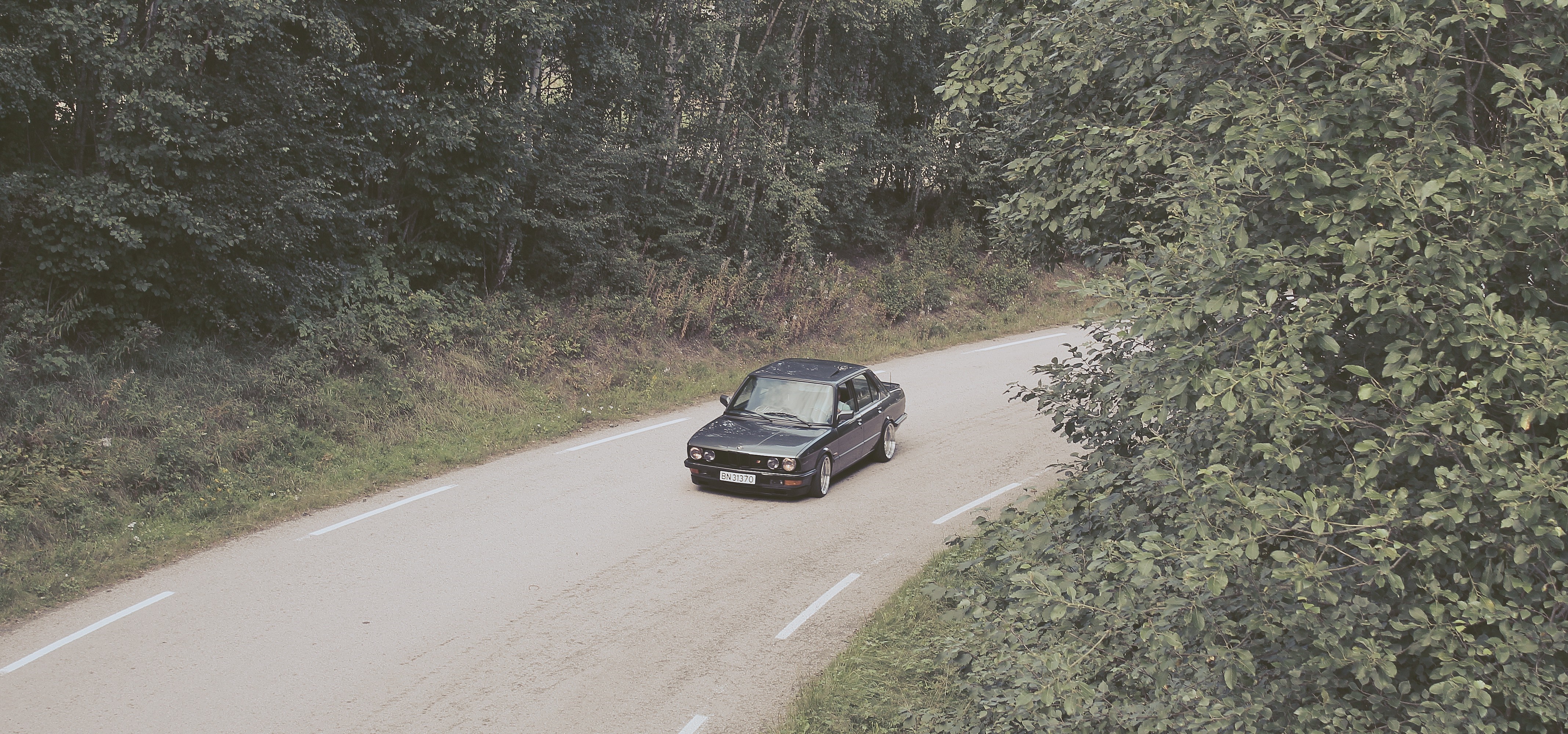 Dark BMW E28 driving on a winding road in Norway HD Wallpaper