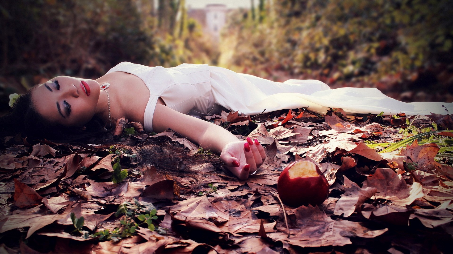 Woman in white dress lying on autumn leaves with an apple HD Wallpaper