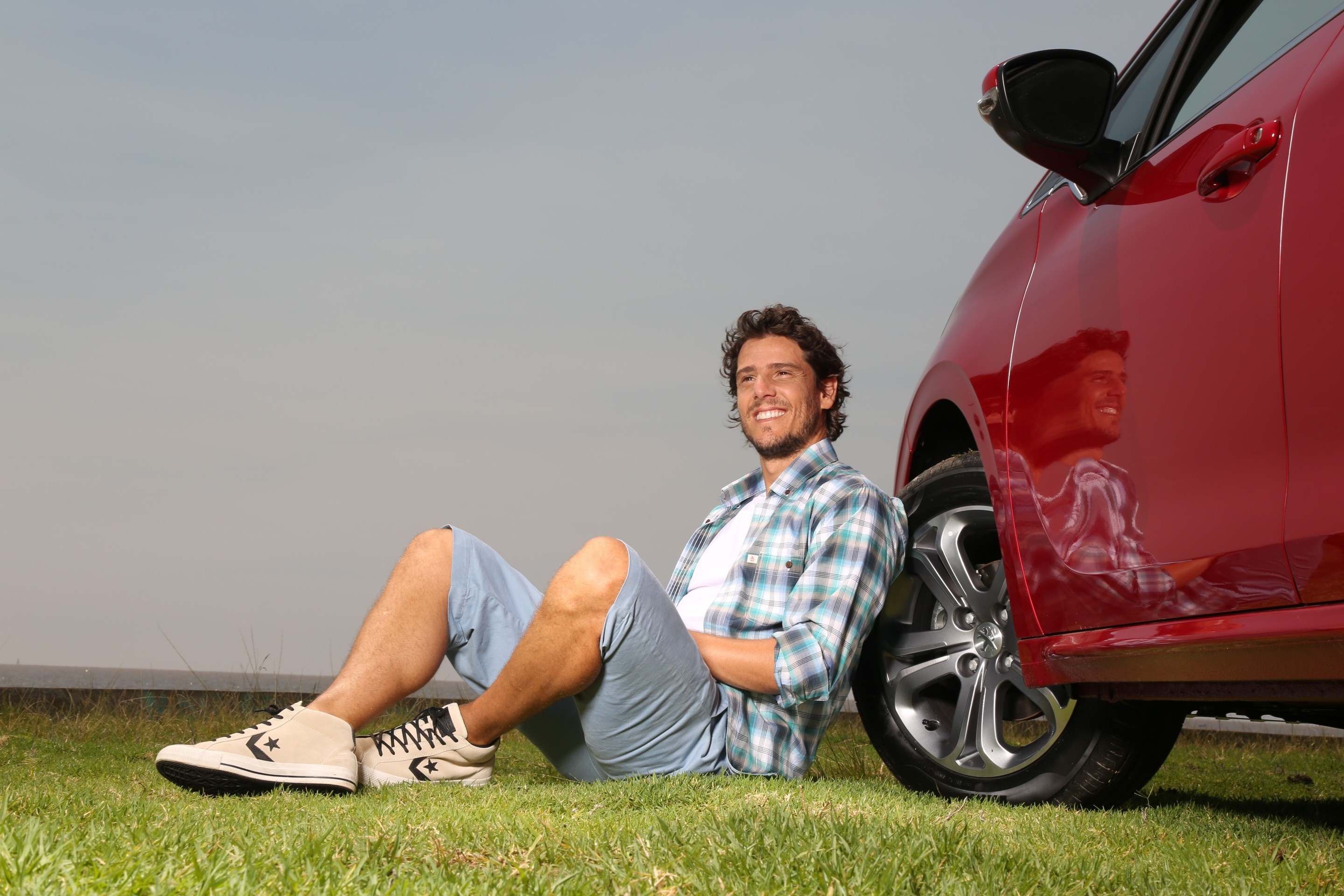 Man sitting by a red car on grass HD Wallpaper