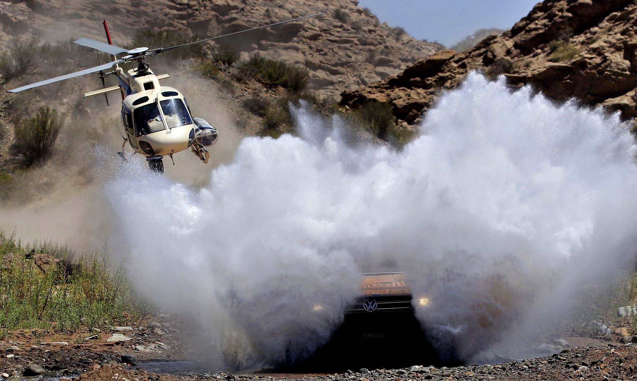Helicopter flies over a car splashing through water in a rocky canyon HD Wallpaper