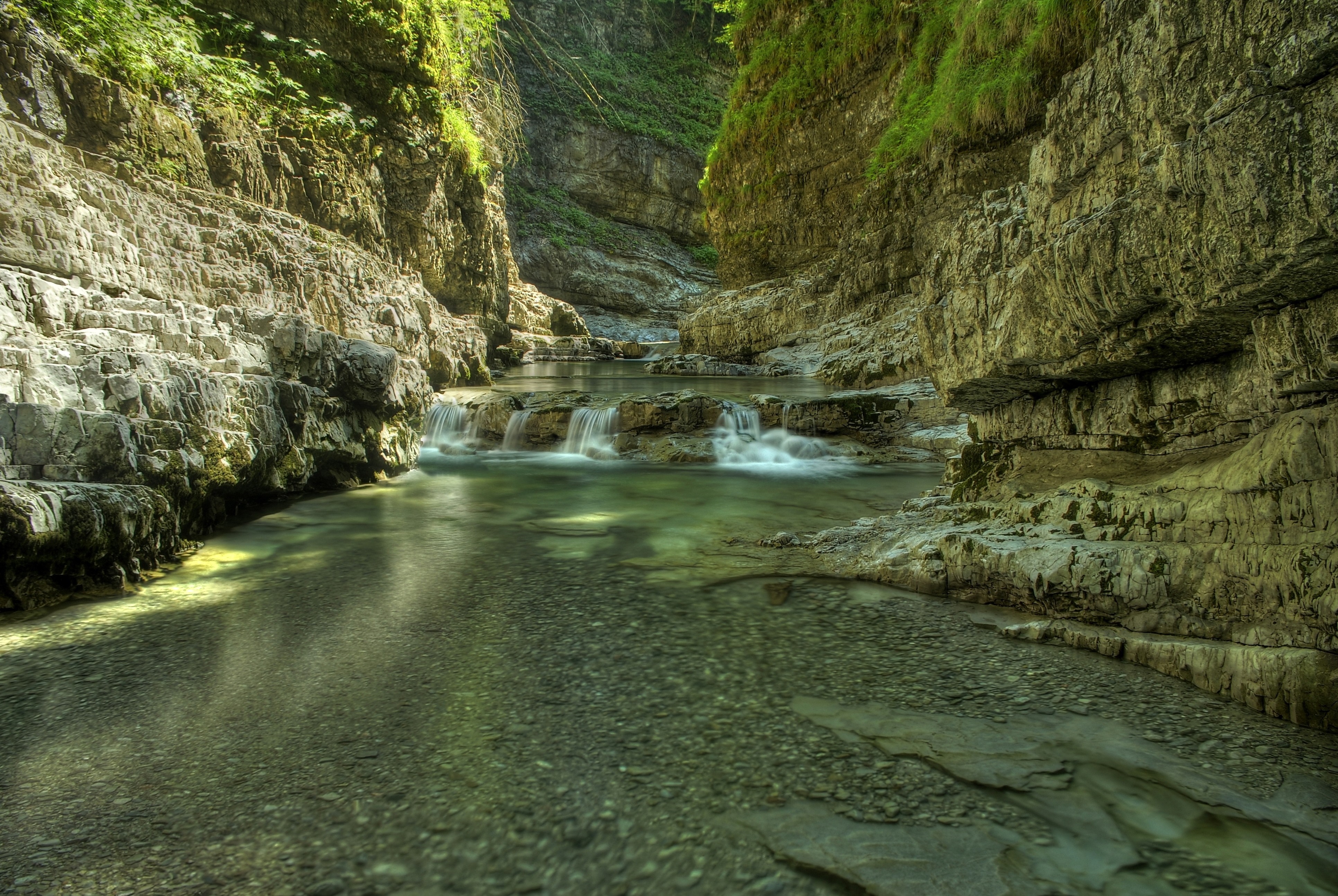 A clear river flows through a rocky canyon with lush green vegetation. HD Wallpaper