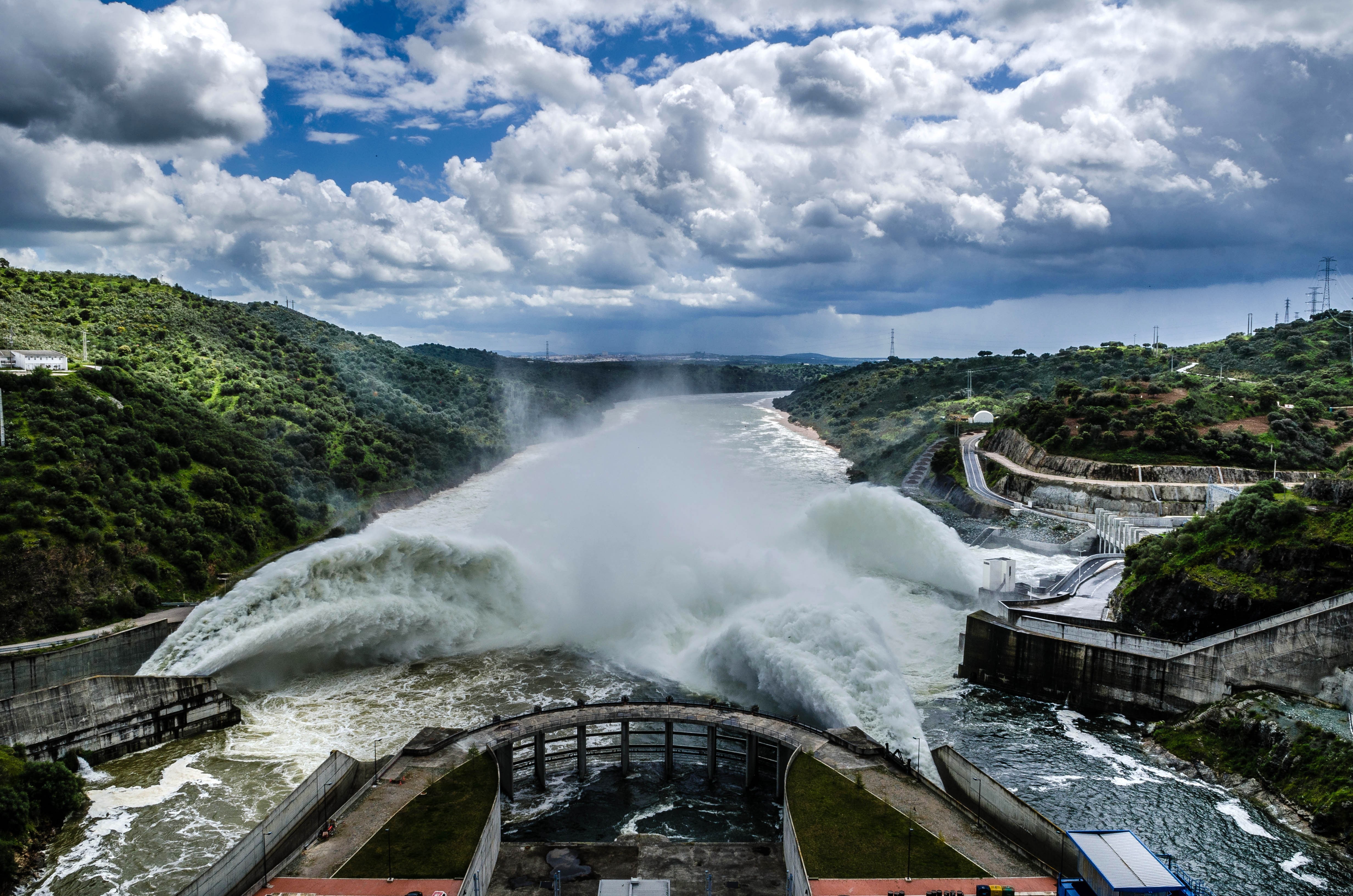 Water gushing from a dam into a river under a cloudy sky HD Wallpaper