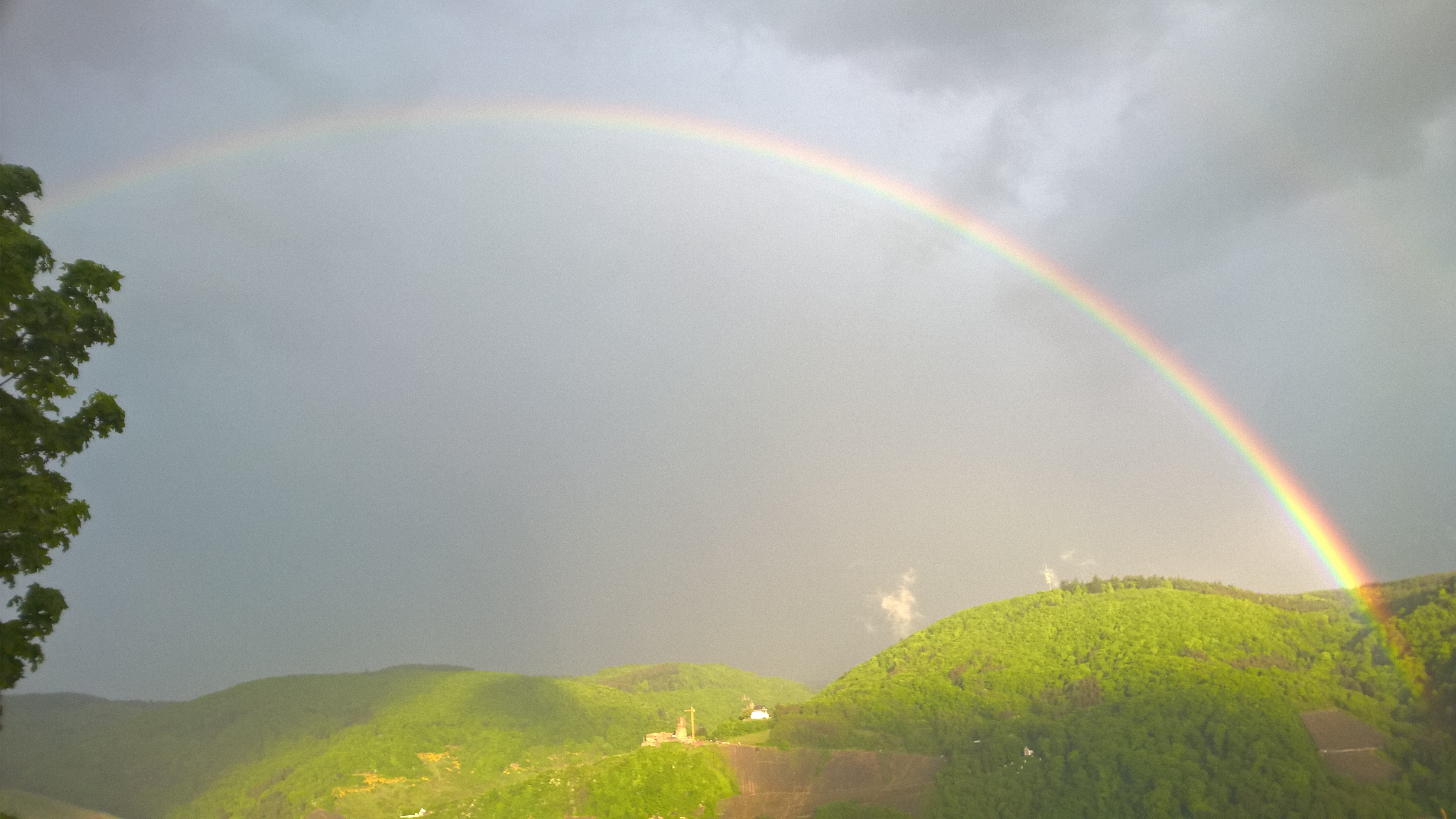 Rainbow over green mountains under a cloudy sky HD Wallpaper