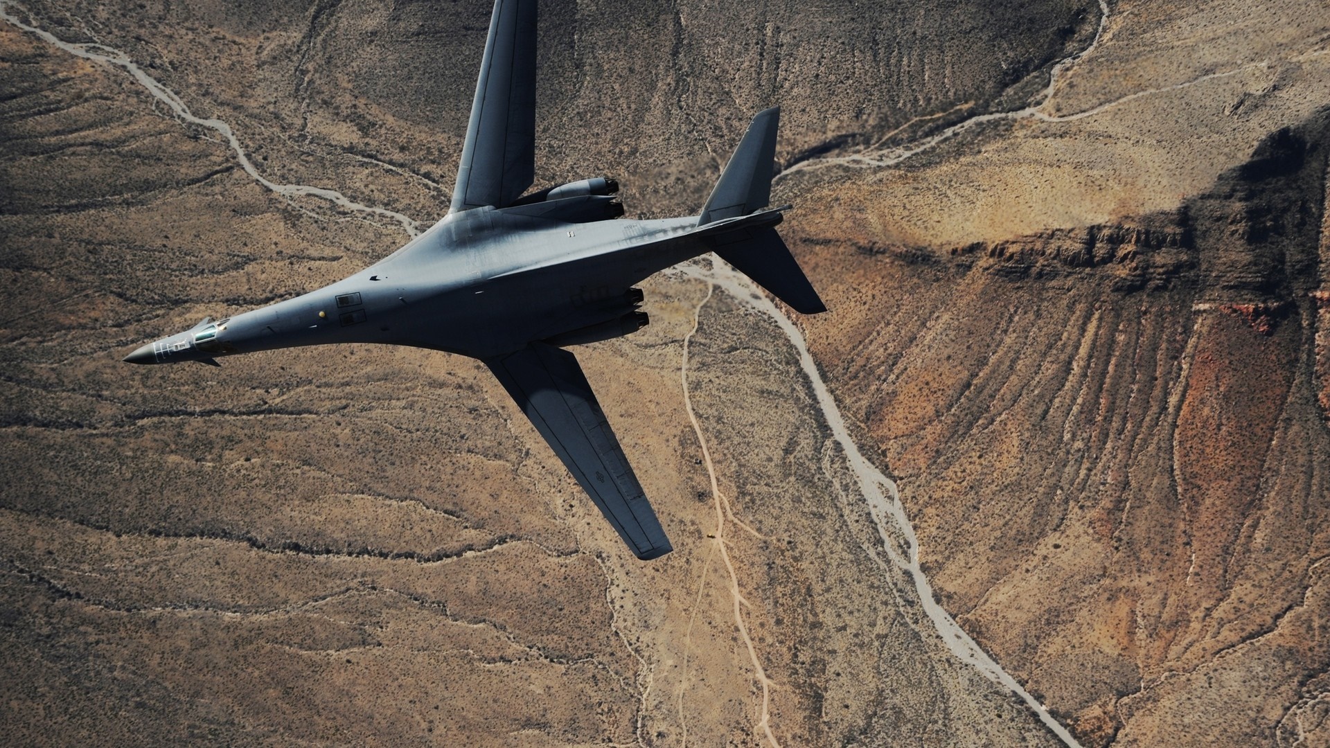 Rockwell B-1 Lancer bomber flying over desert terrain HD Wallpaper