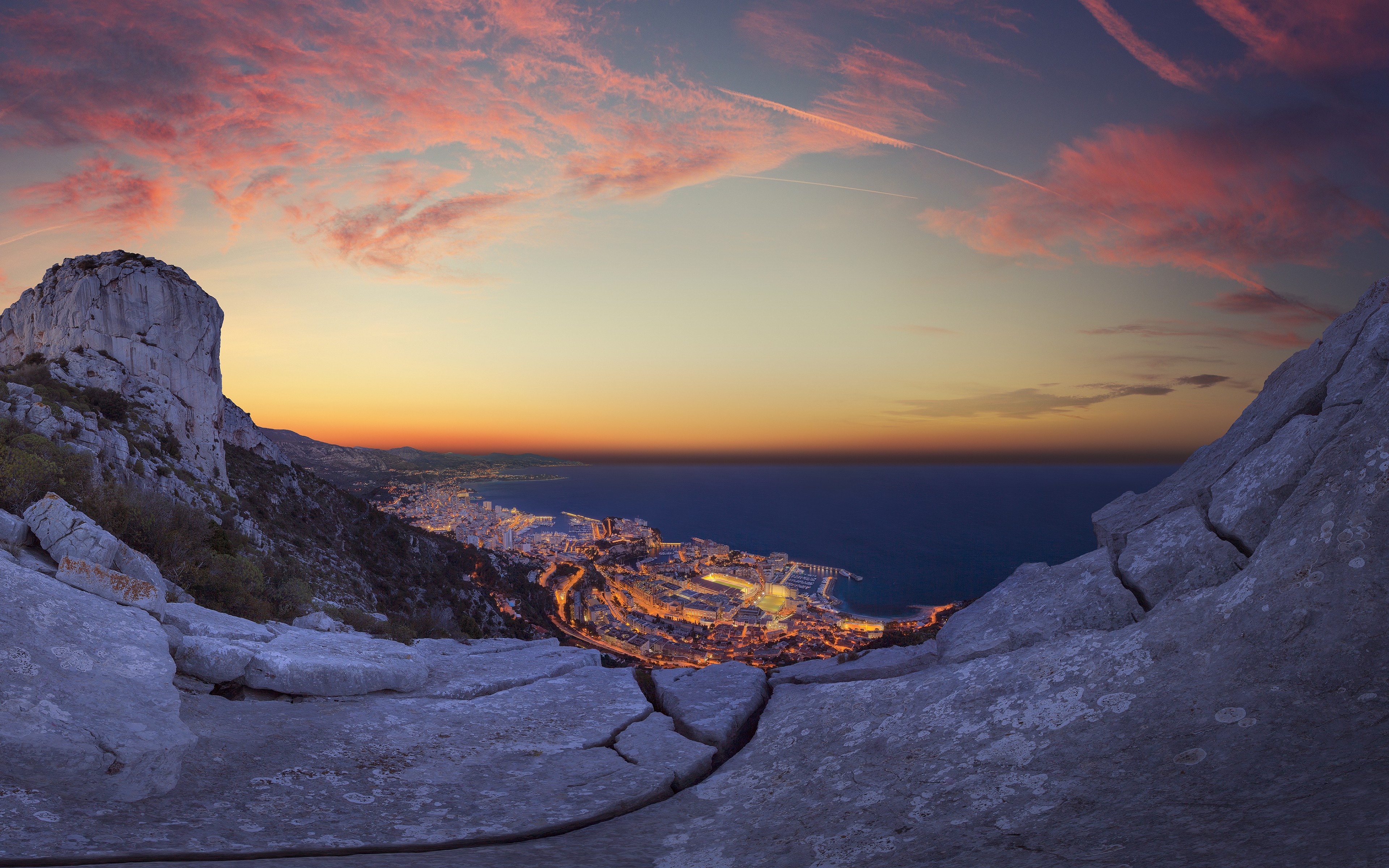 City lights by the sea at sunset from a rocky viewpoint HD Wallpaper