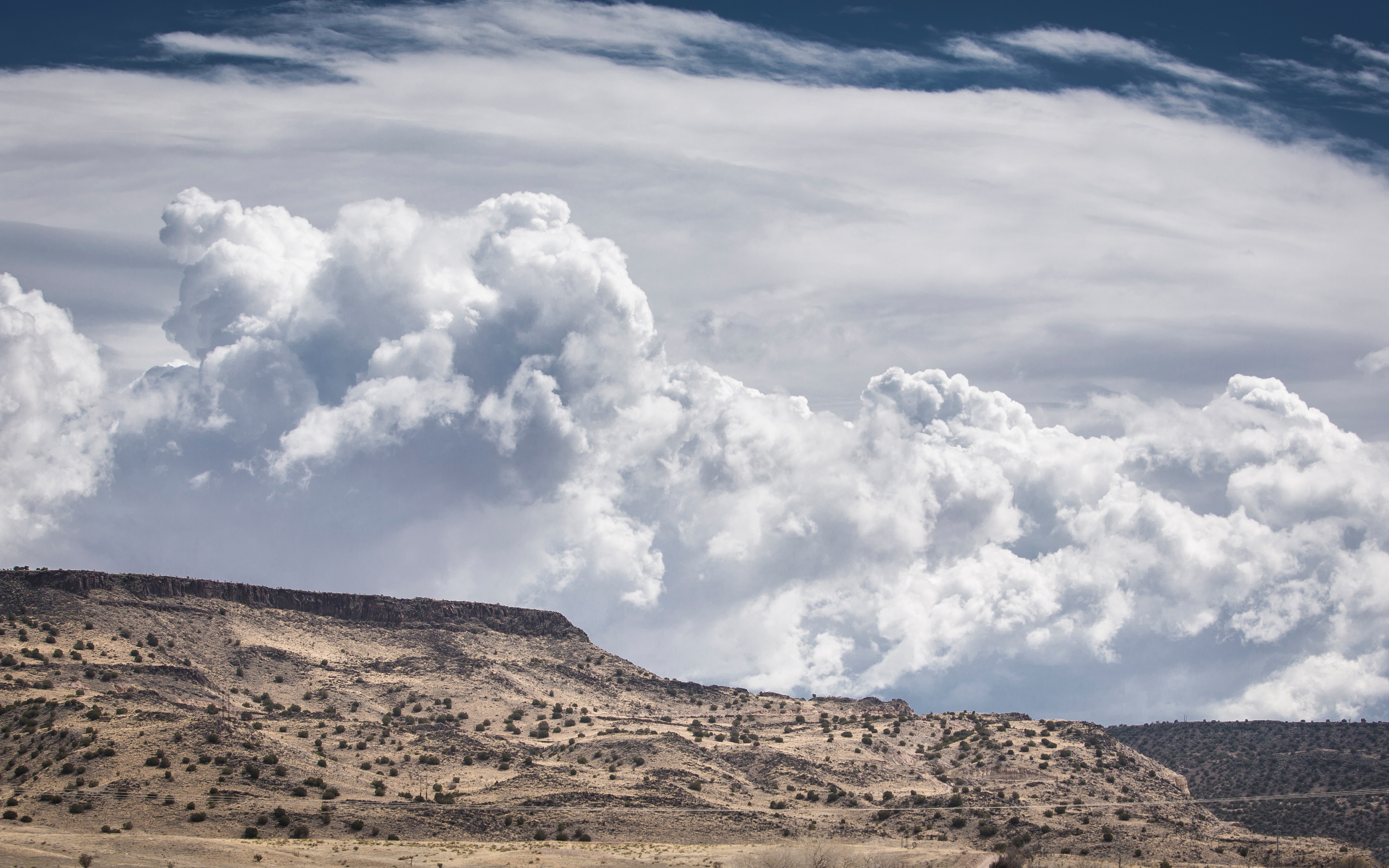 Cumulus clouds over a desert plateau with sparse vegetation HD Wallpaper