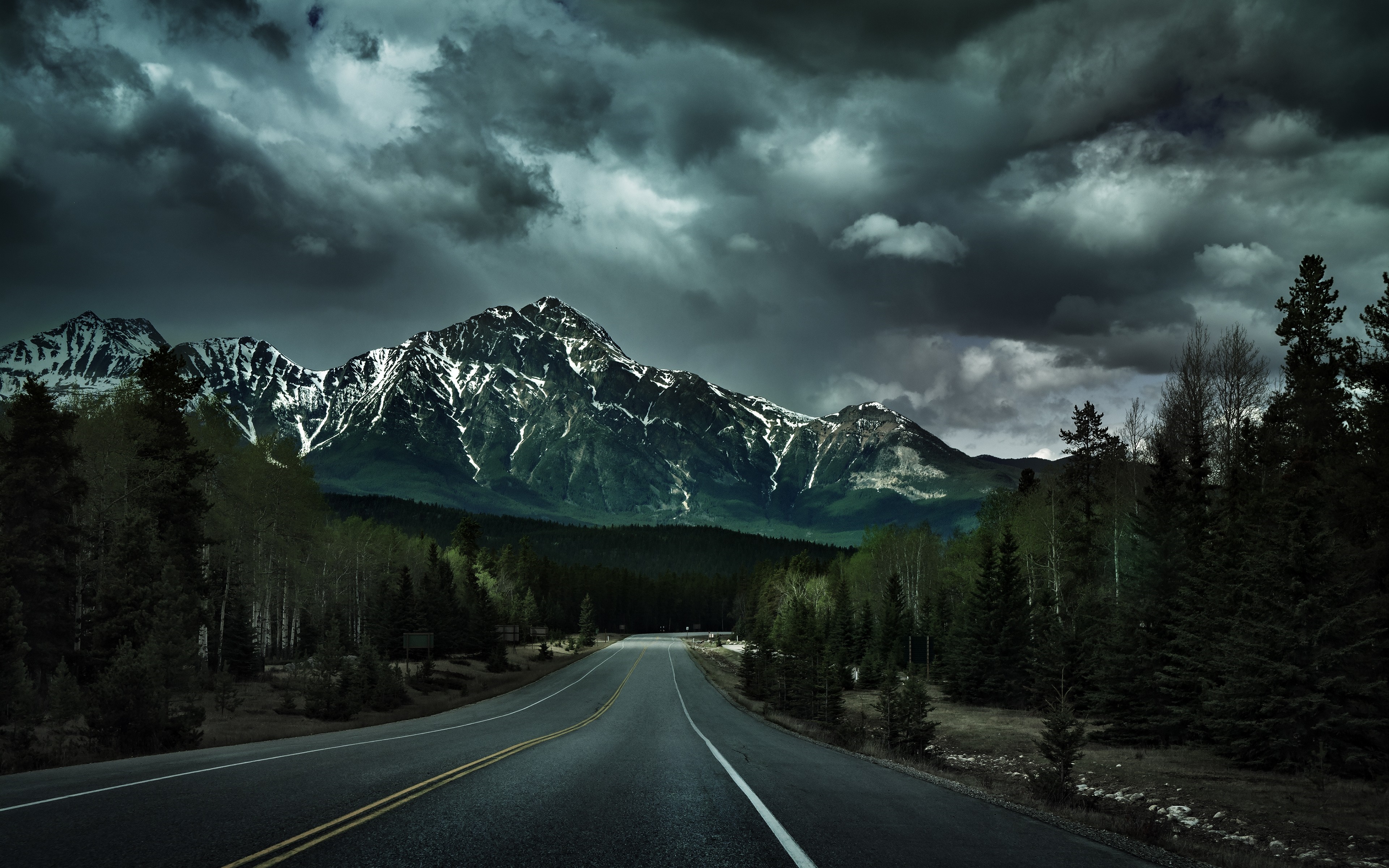 Road leading to snow-capped mountains under stormy clouds HD Wallpaper
