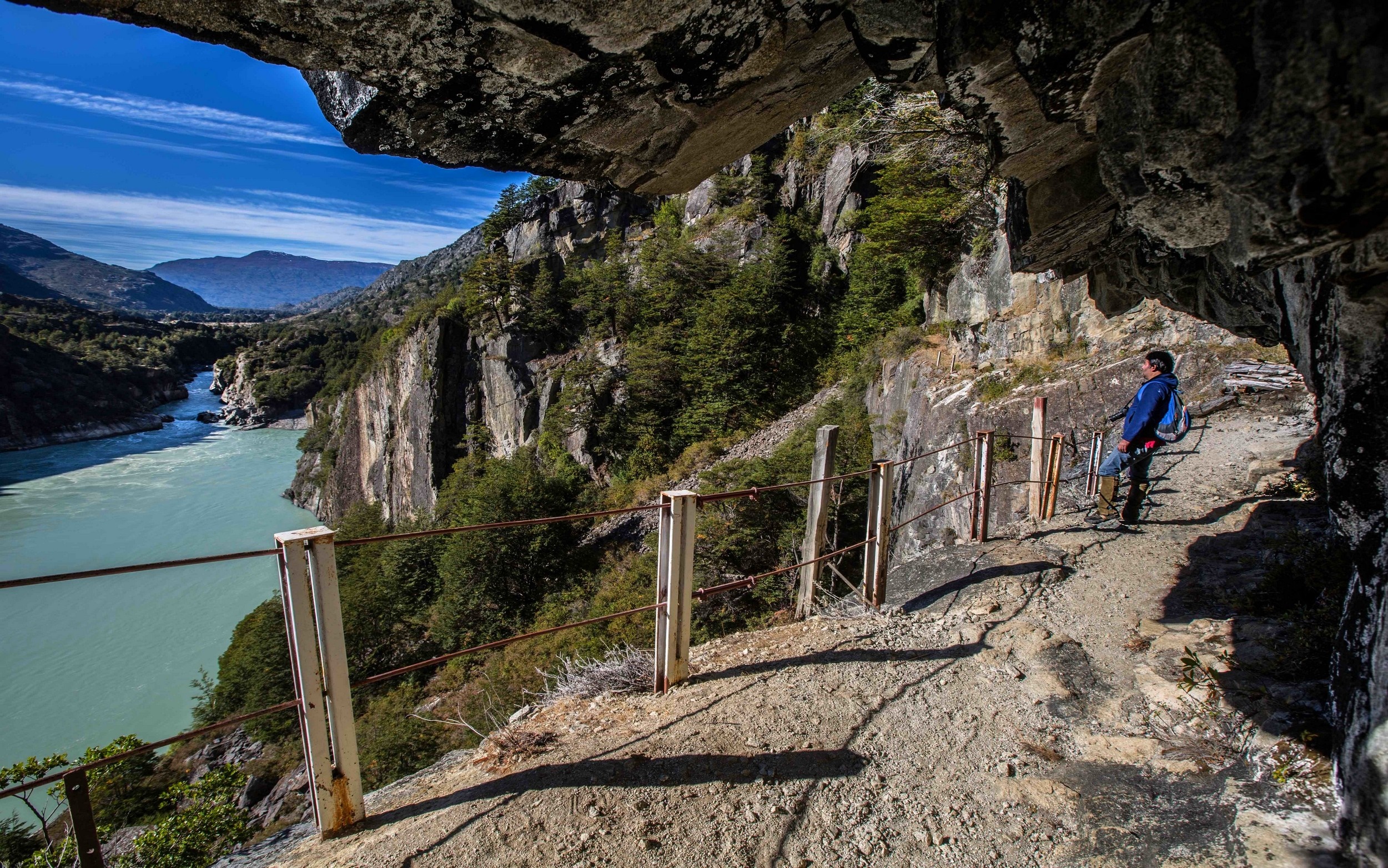 Hiker on a cliffside path overlooking a turquoise river in Chile HD Wallpaper