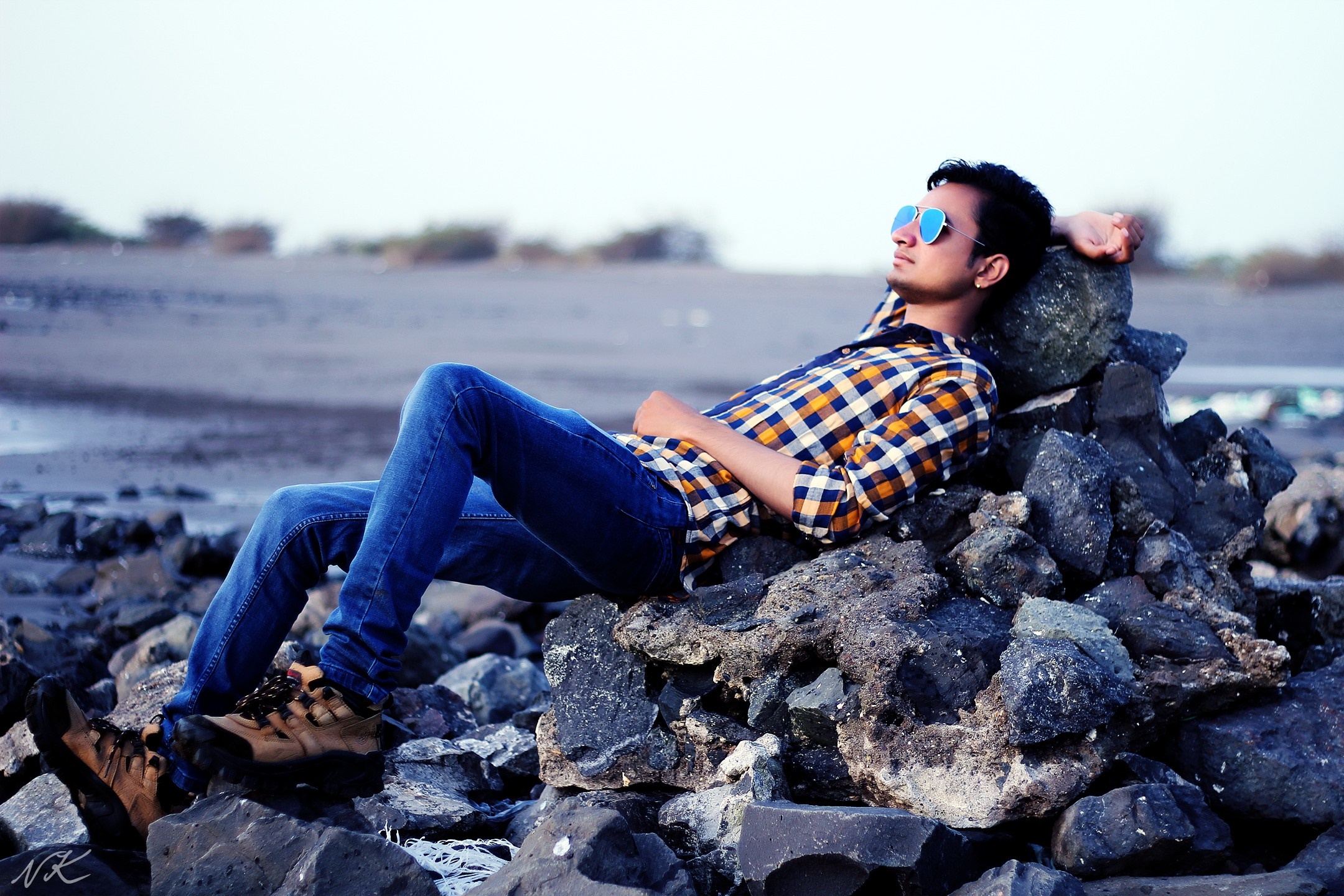 Man in plaid shirt and sunglasses relaxing on rocks HD Wallpaper