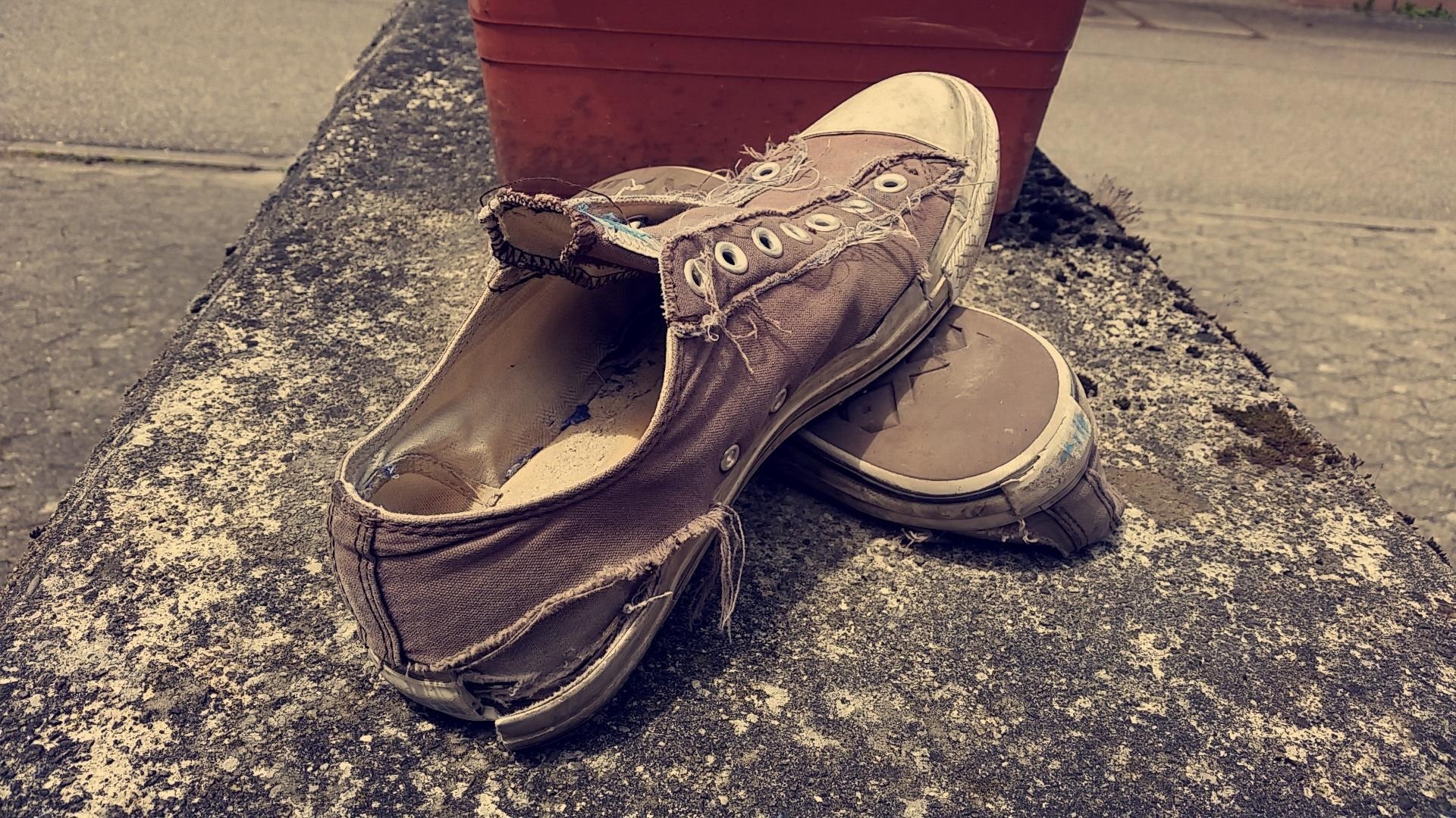 Pair of worn-out canvas sneakers on a concrete ledge HD Wallpaper