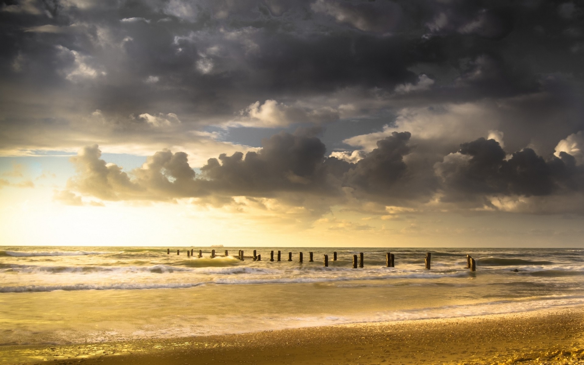 Wooden posts in the sea at sunset with dramatic clouds HD Wallpaper