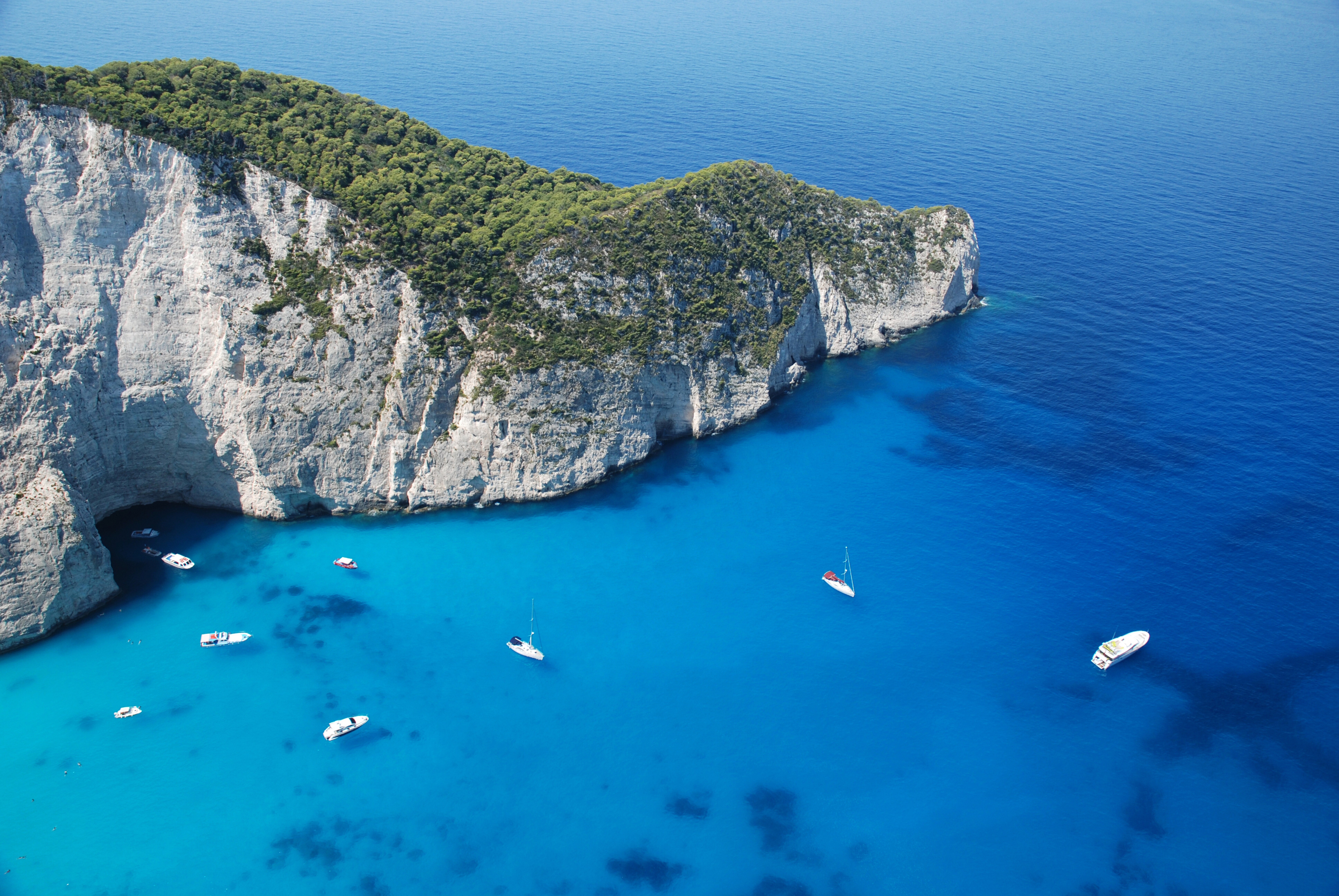 Boats in a turquoise bay next to a forested cliff HD Wallpaper