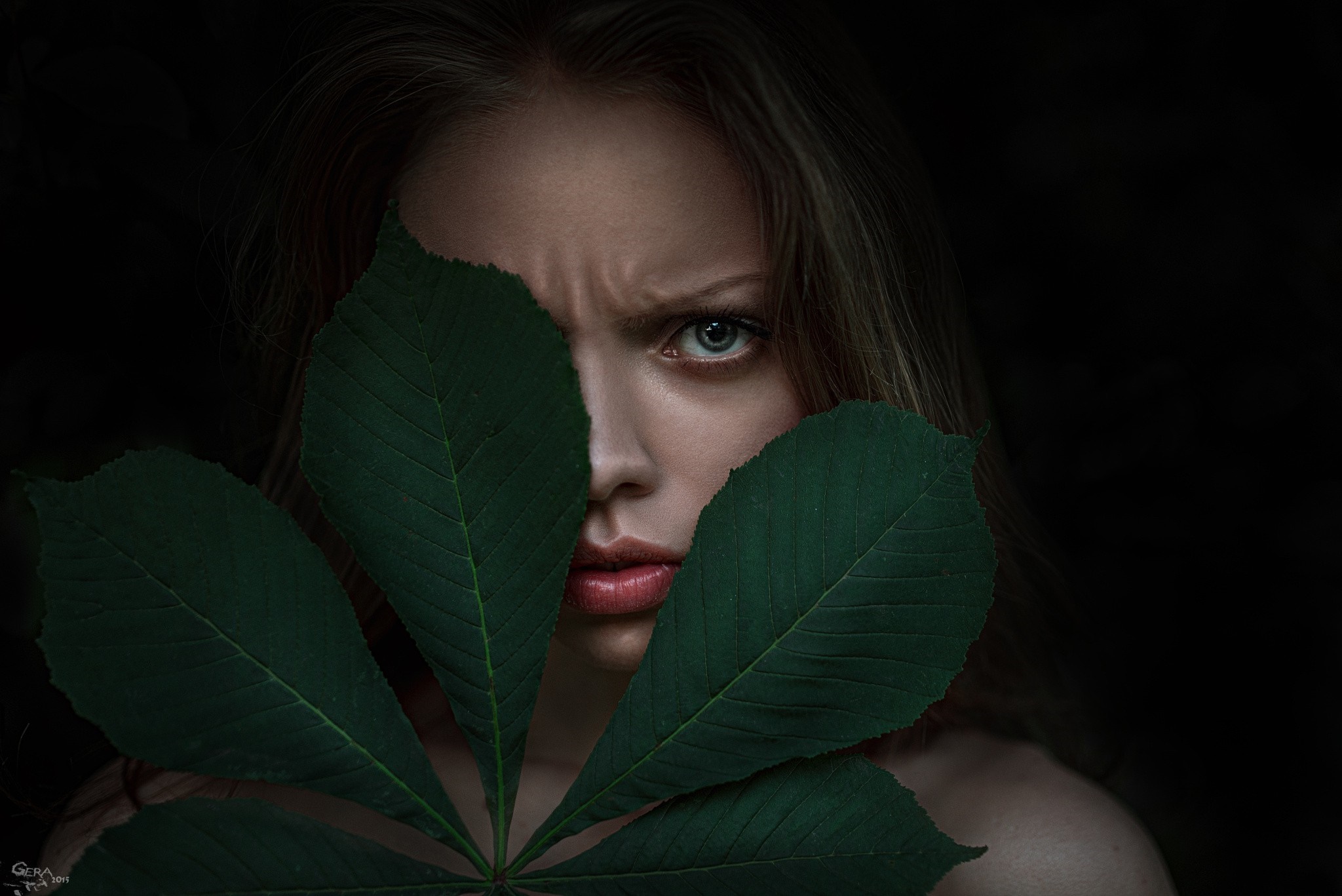 Woman's face partially hidden by green leaves HD Wallpaper