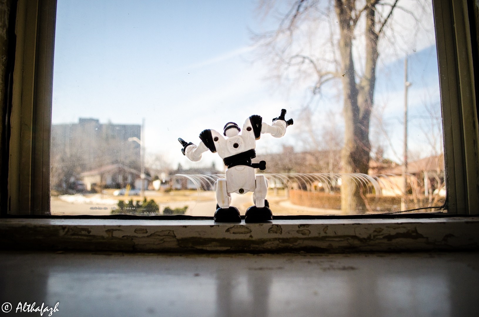 Robot toy on a windowsill with a view of houses and trees HD Wallpaper