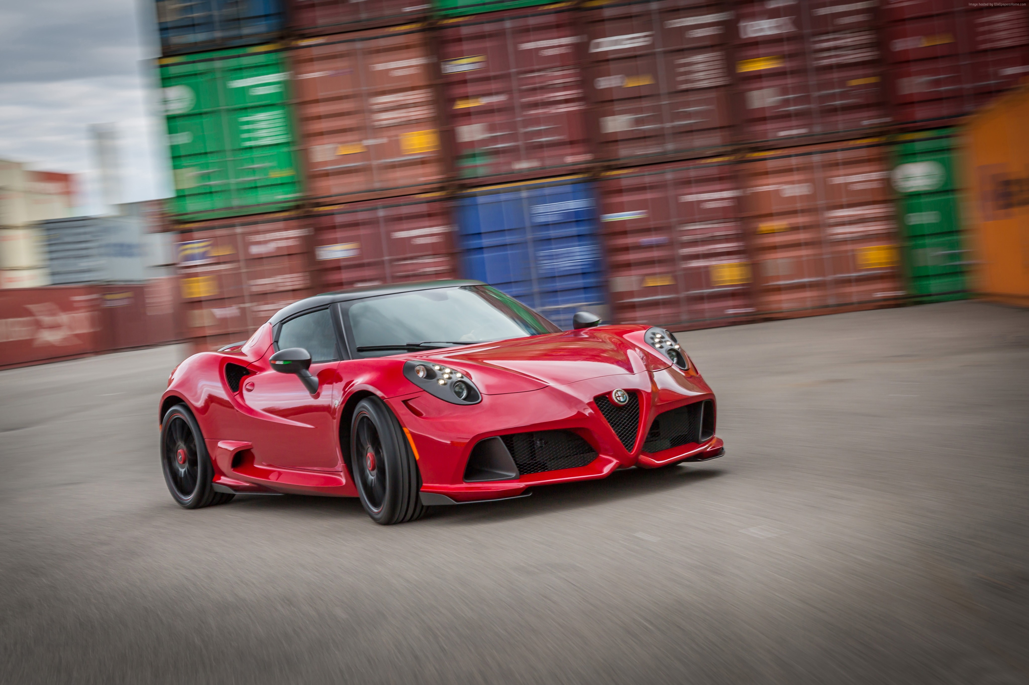 Red Alfa Romeo 4C sports car driving past shipping containers HD Wallpaper