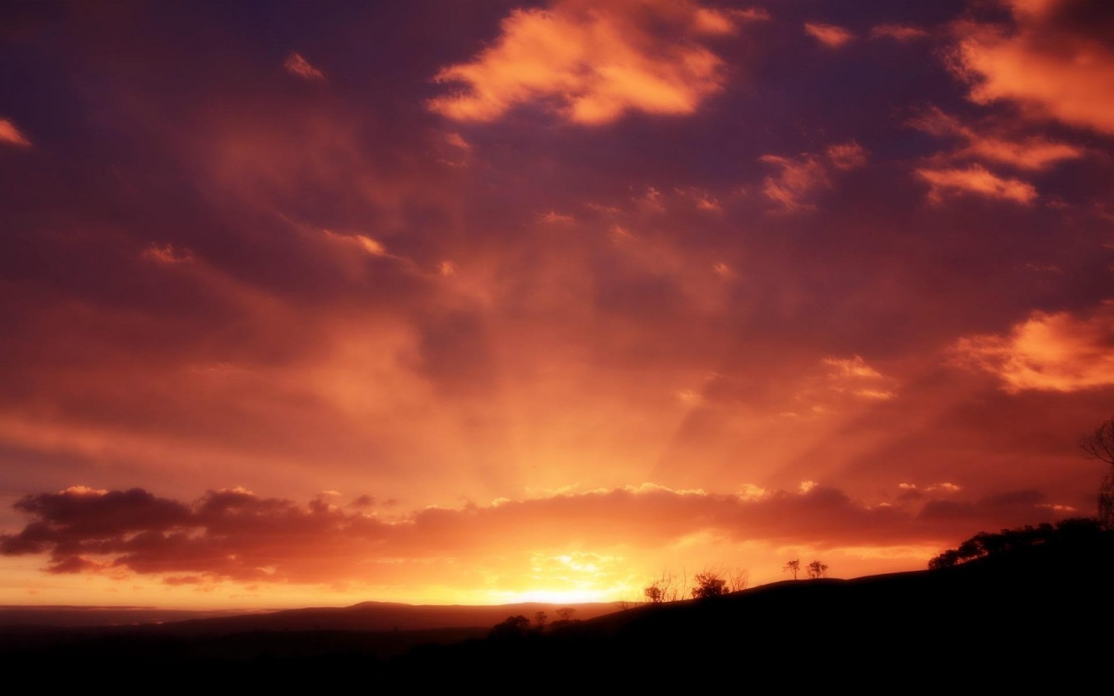 Sunset with sun rays over a silhouetted landscape HD Wallpaper