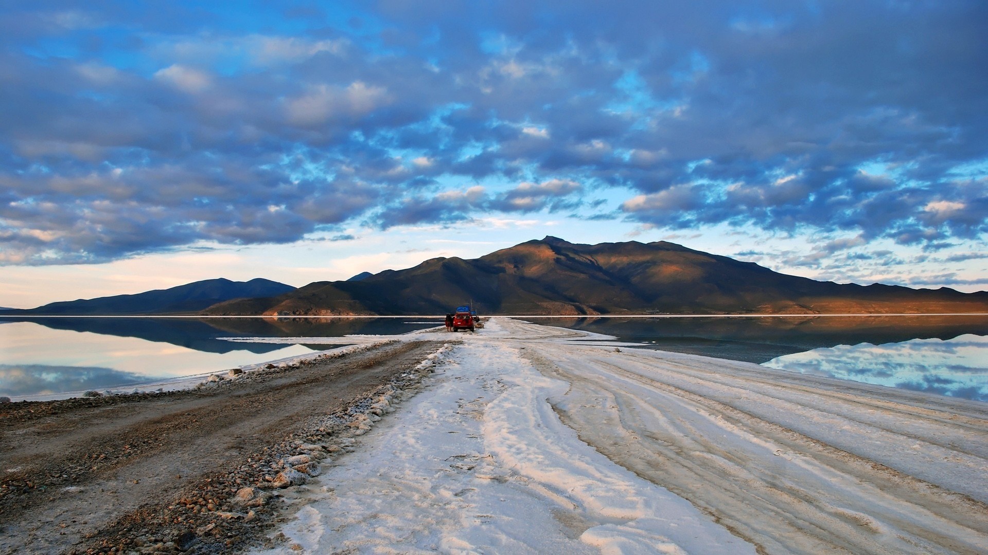 Red car on a salt flat with mountains in the background HD Wallpaper