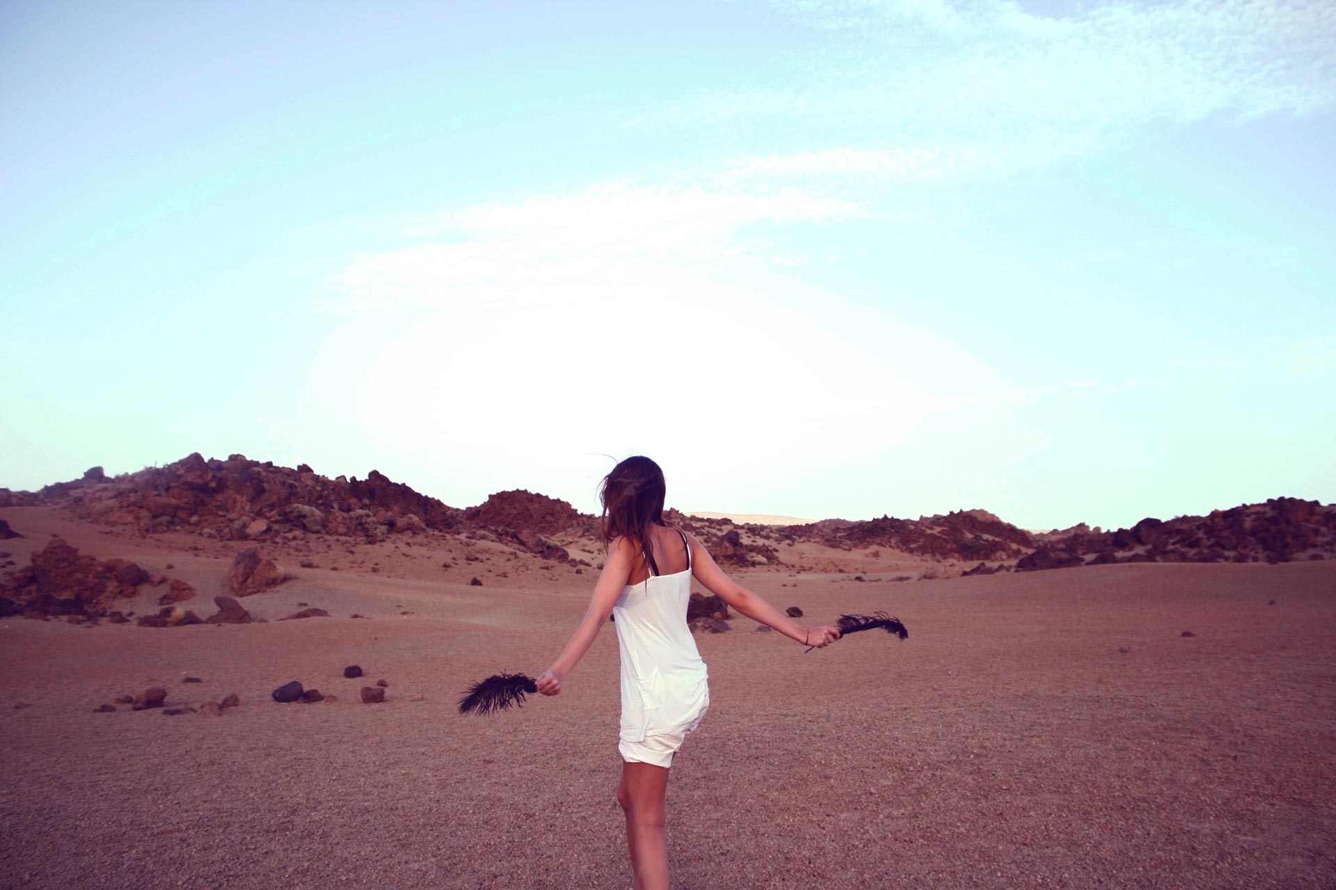 Woman in white dress holding feathers in desert landscape HD Wallpaper