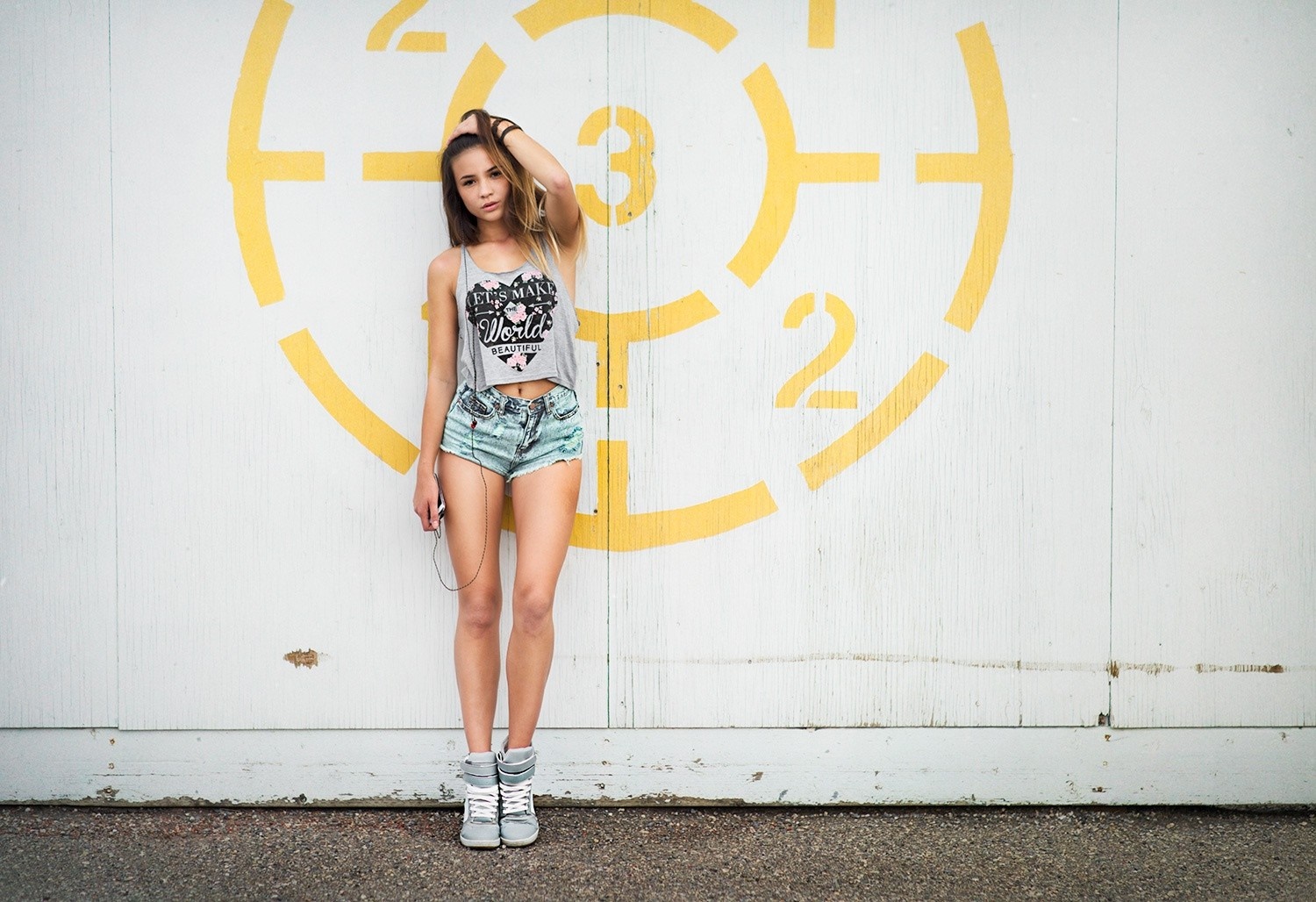 Woman in jean shorts and tank top leaning against a wall HD Wallpaper