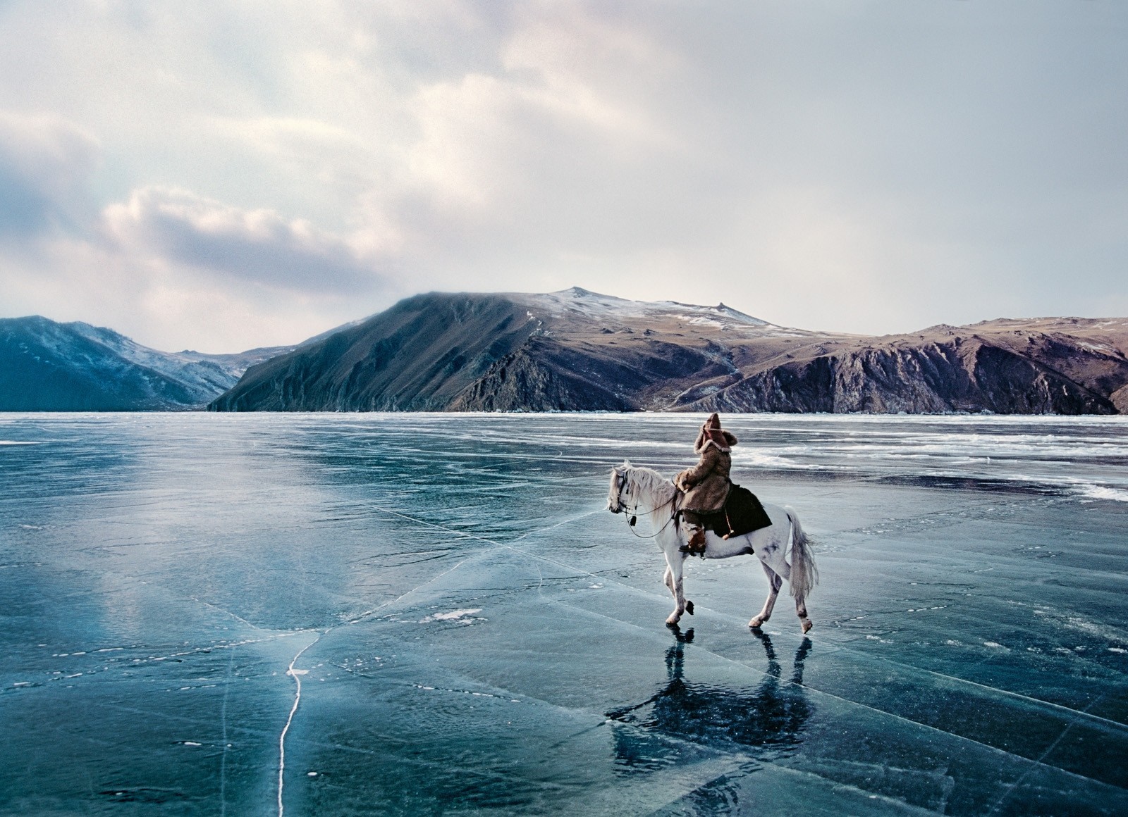 Person riding a white horse on frozen lake with mountains HD Wallpaper