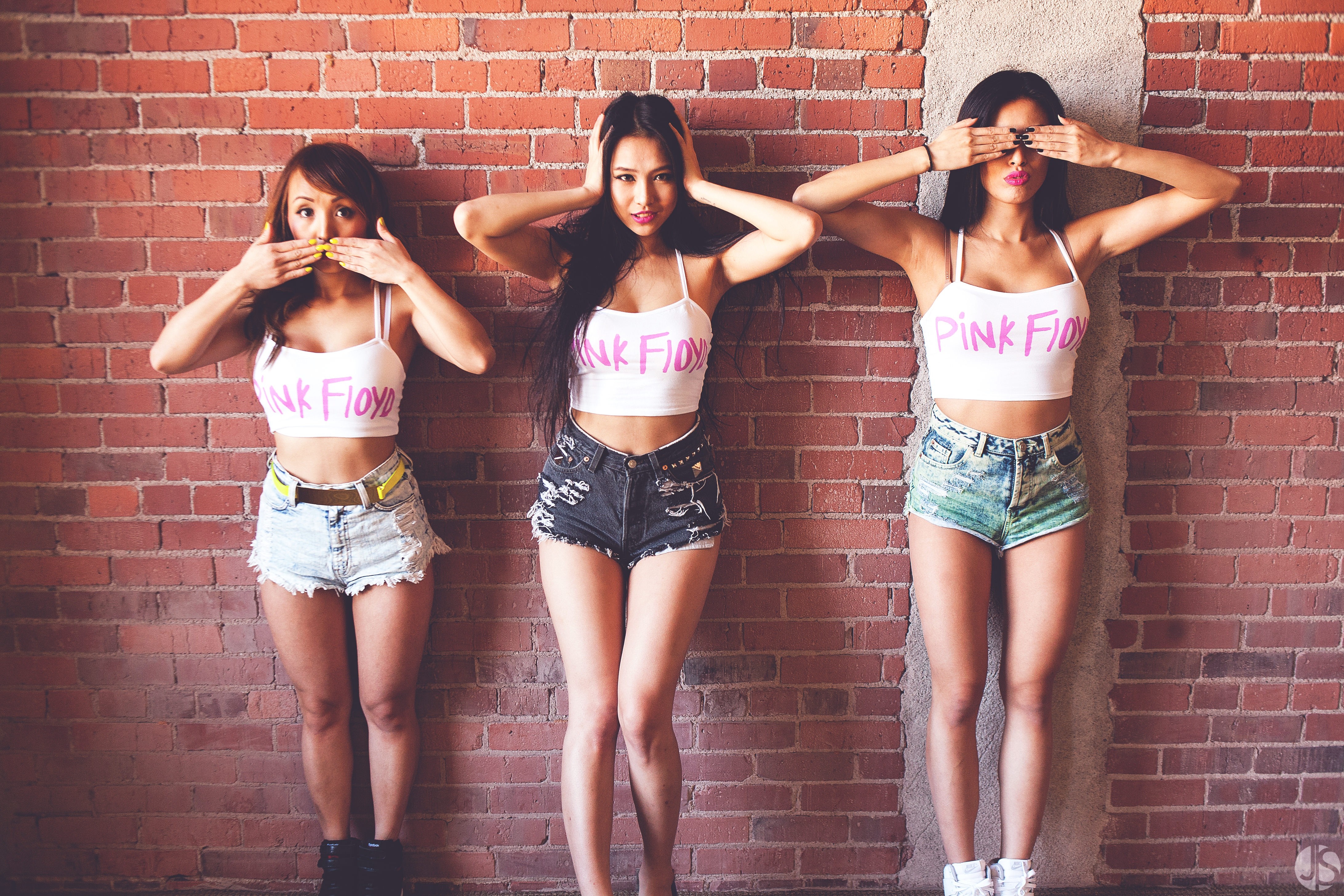 Three women in crop tops and jean shorts posing against a brick wall HD Wallpaper