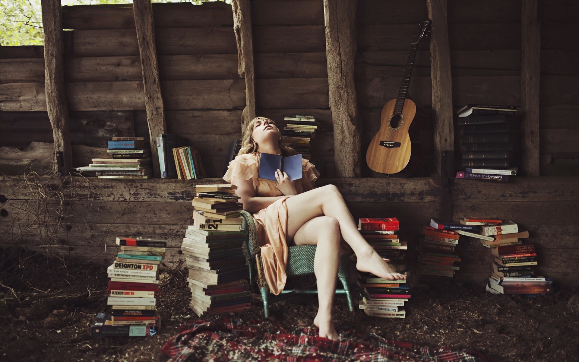 Woman reading a book in a rustic setting with books and guitar HD Wallpaper