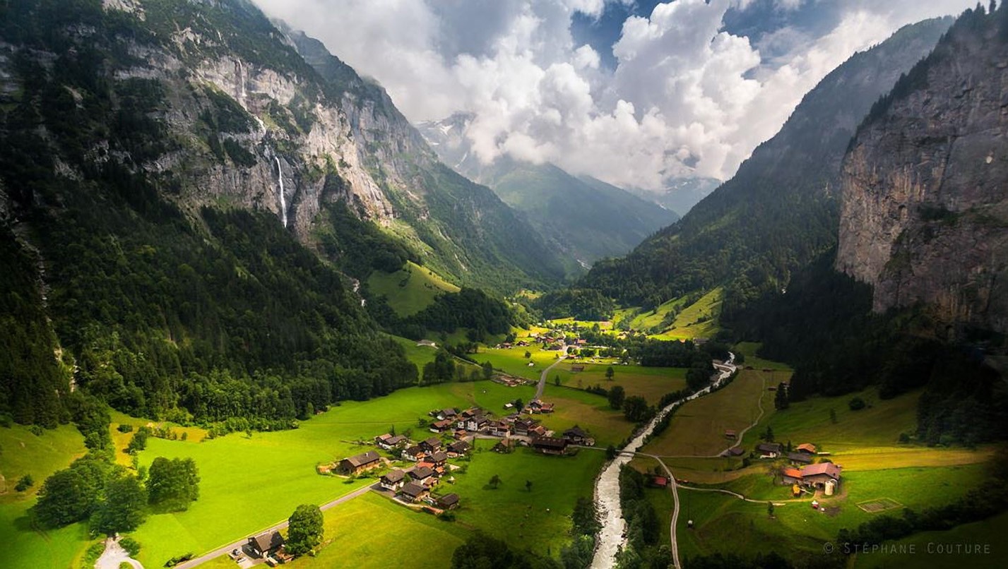 Aerial view of a valley with a village and waterfall in the Alps HD Wallpaper