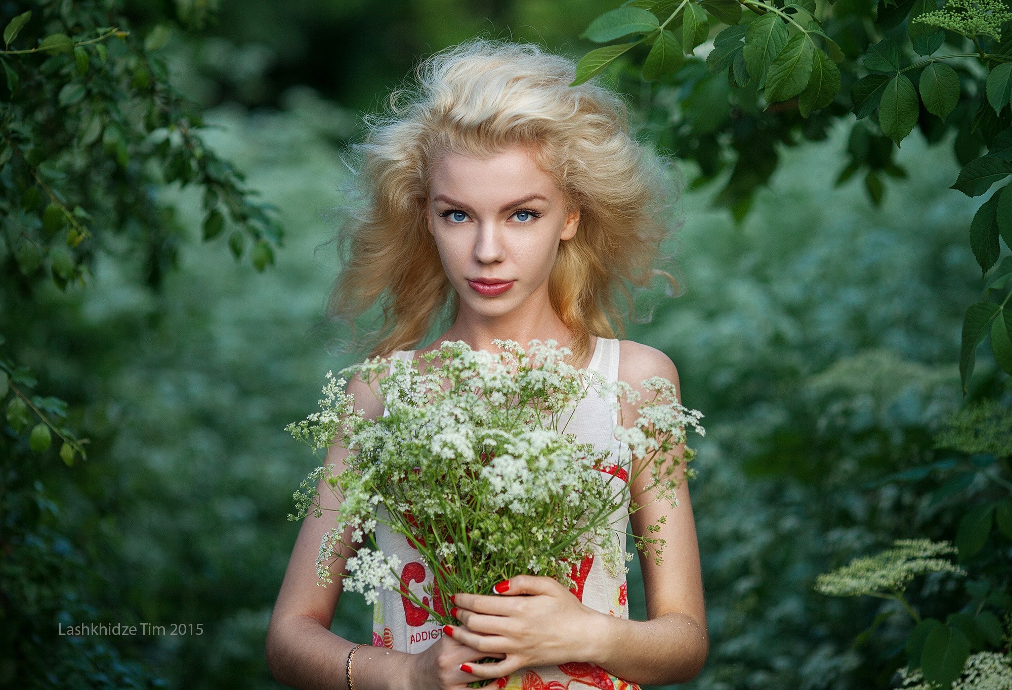 Woman with blonde hair holding flowers in a forest HD Wallpaper
