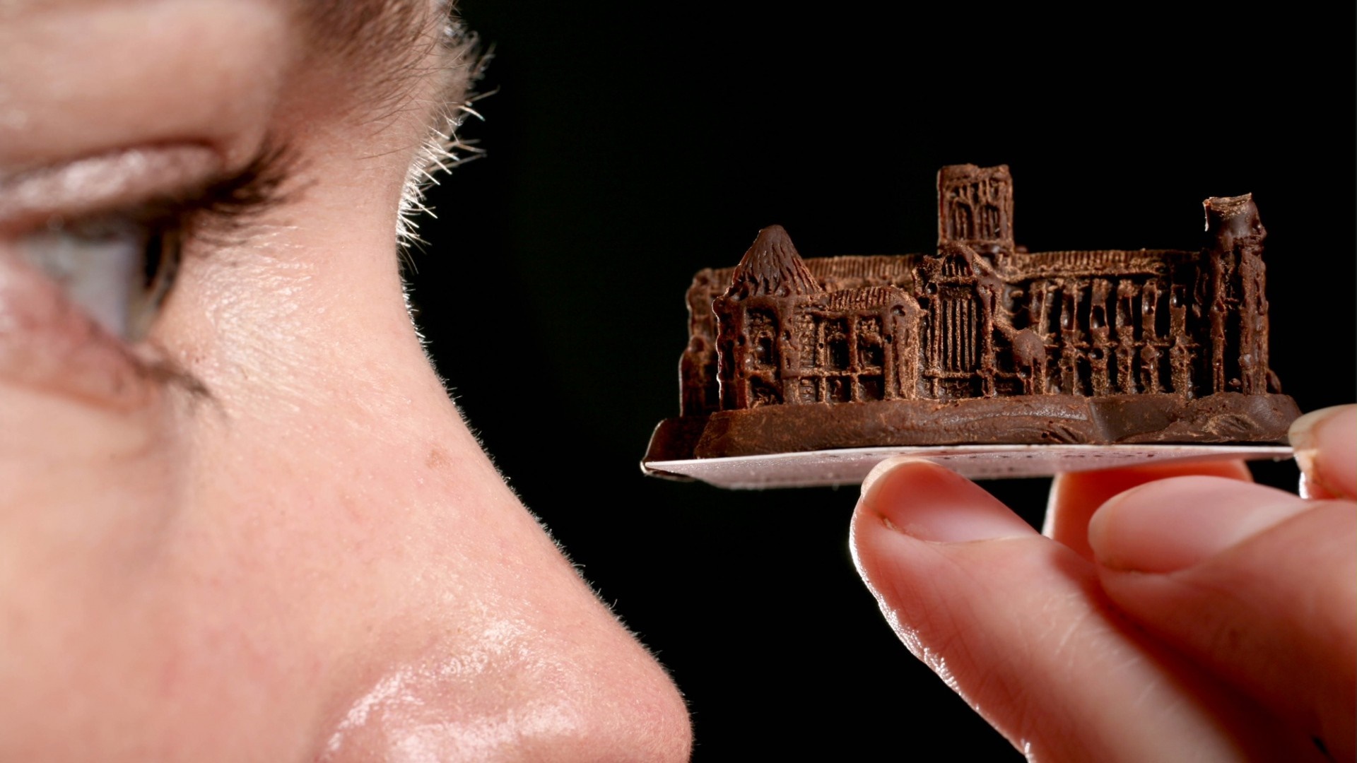 Close-up of a woman's face looking at a chocolate miniature building HD Wallpaper