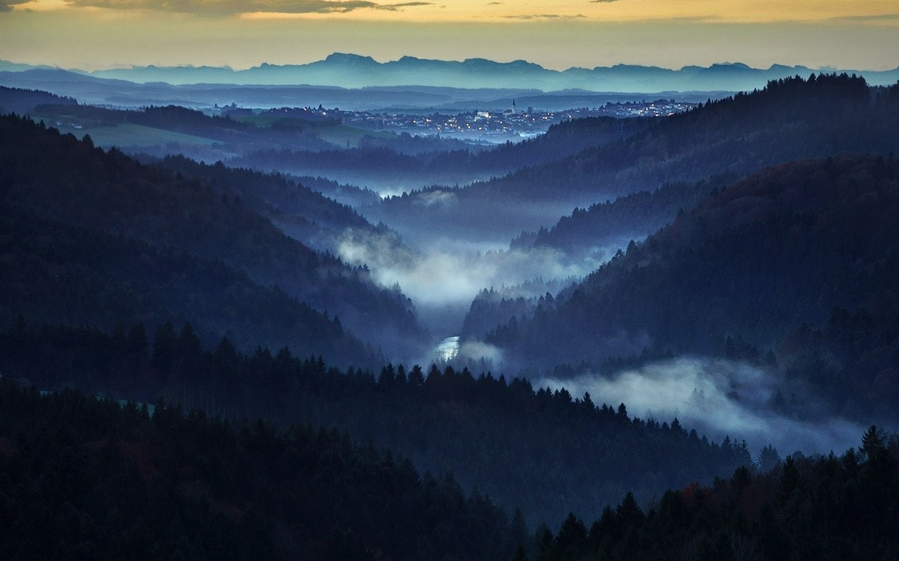Misty valley with forest and distant town at dawn HD Wallpaper