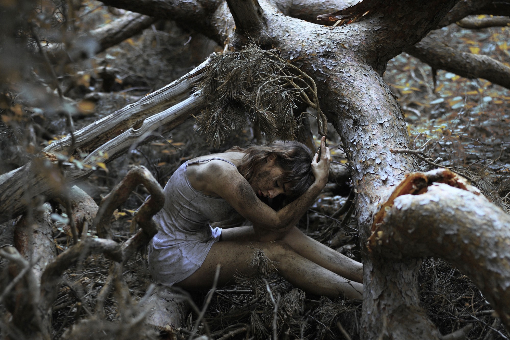 Woman covered in mud sitting amongst tree roots HD Wallpaper