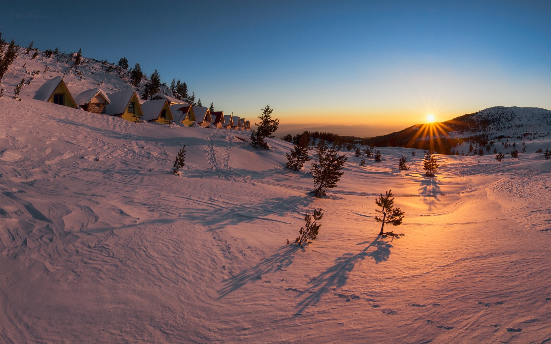 Winter sunset over snowy mountain cabins HD Wallpaper