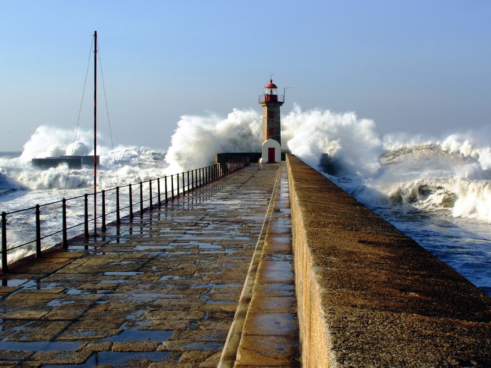 Lighthouse on a pier with large waves crashing HD Wallpaper