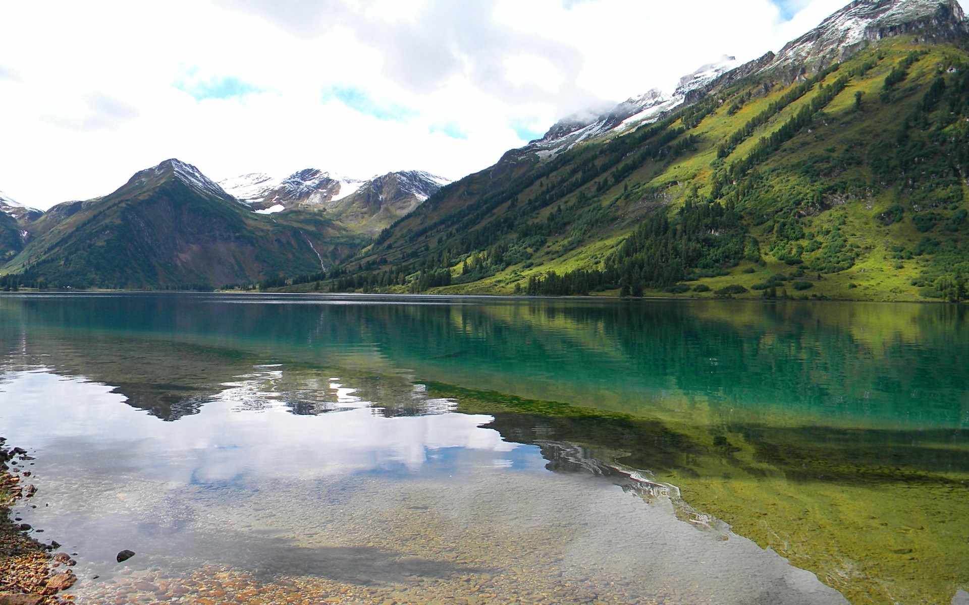 Turquoise mountain lake reflecting snow-capped peaks and green slopes HD Wallpaper