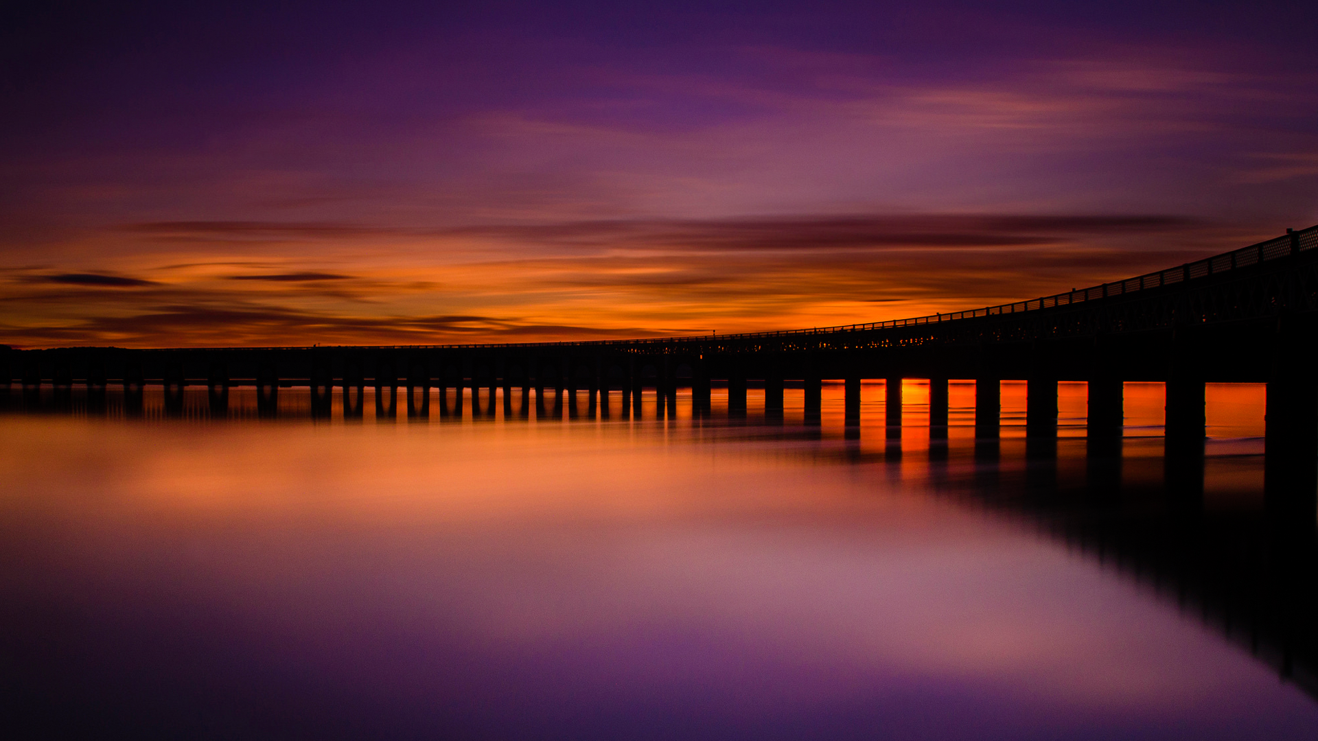 Bridge over water at sunset with colorful sky HD Wallpaper