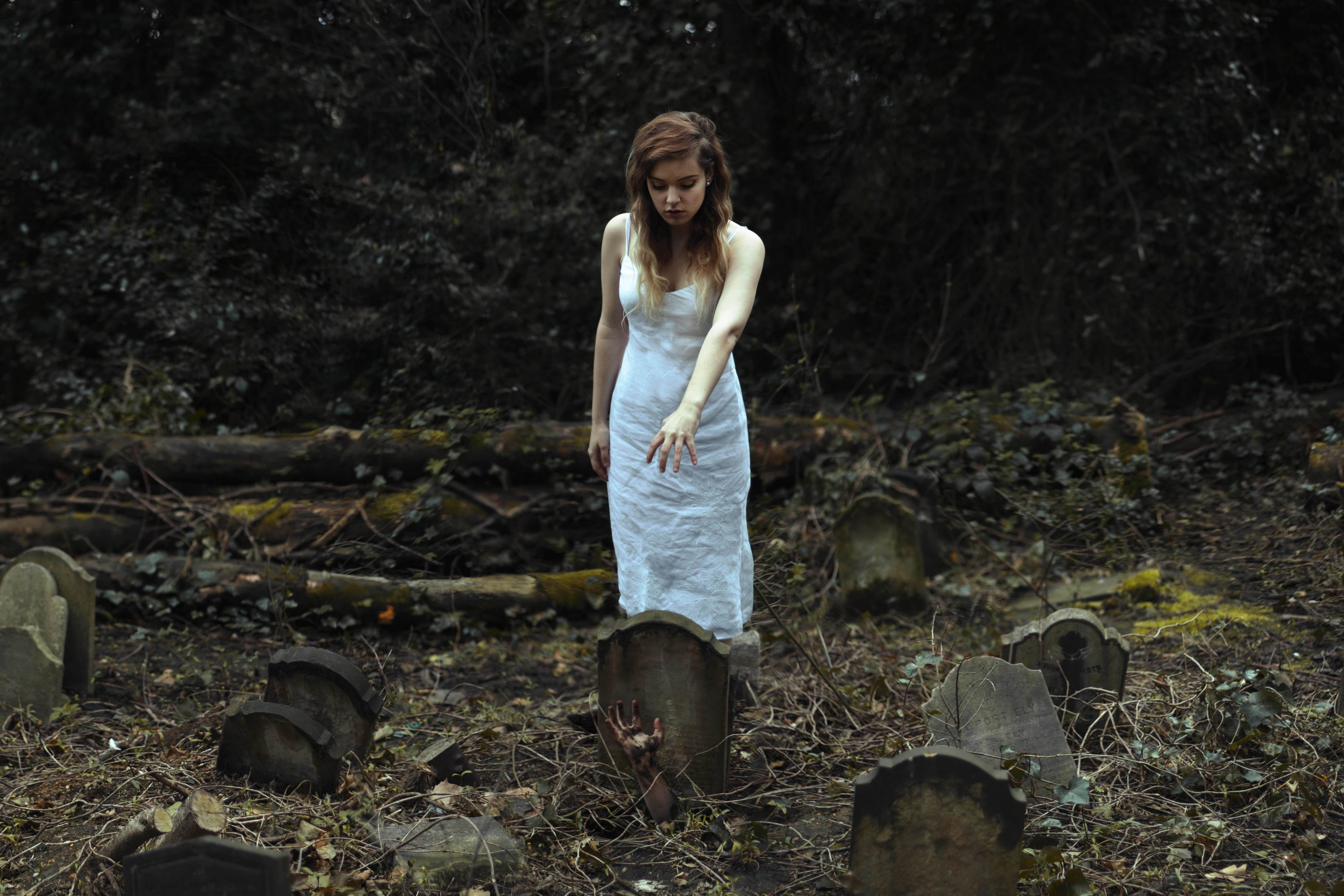 Woman in white dress in a graveyard with a hand emerging from a grave HD Wallpaper